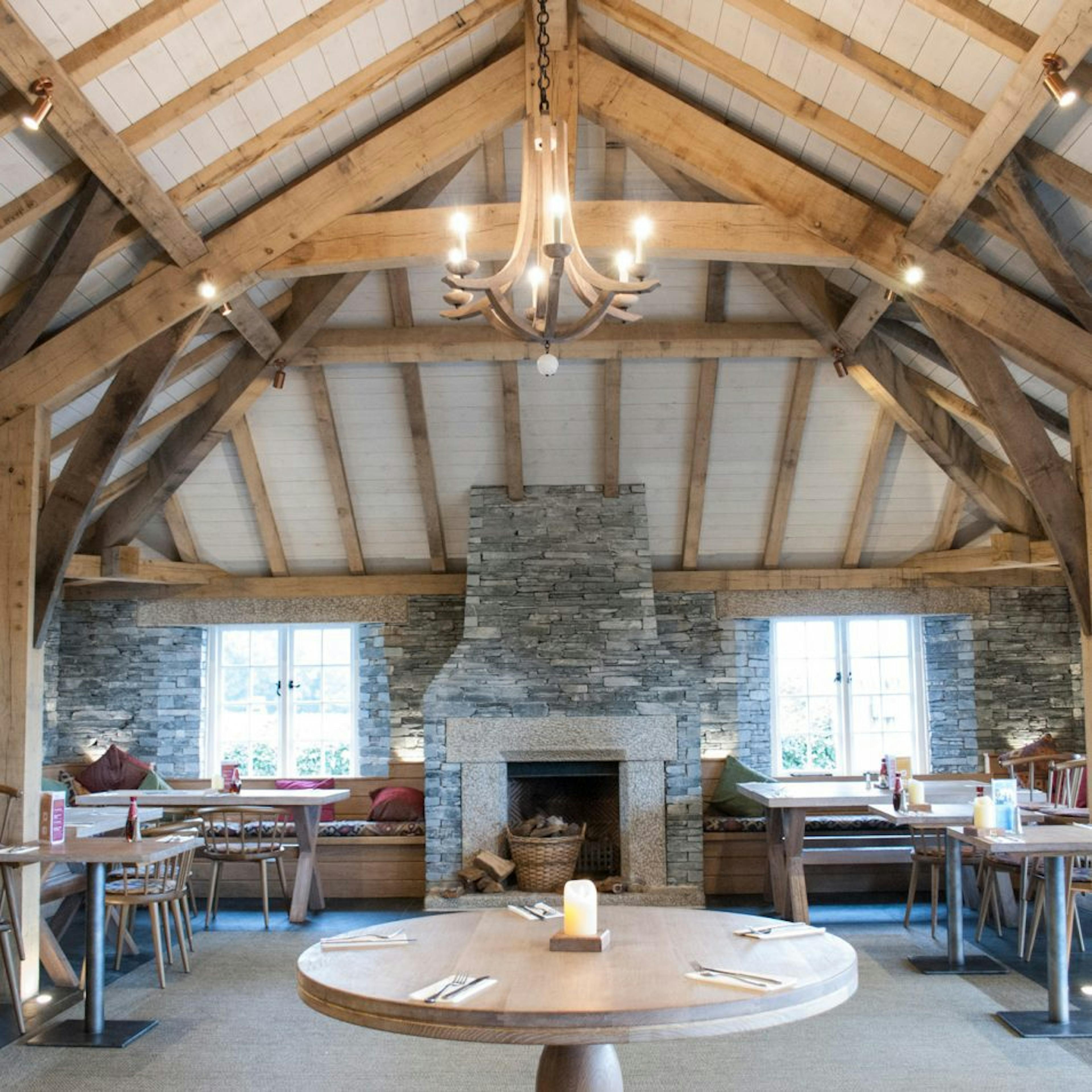 Internal view of Rick Stein's Cornish Arms pub, featuring a structural oak frame with exposed beams and a central fireplace, creating a cozy and rustic atmosphere