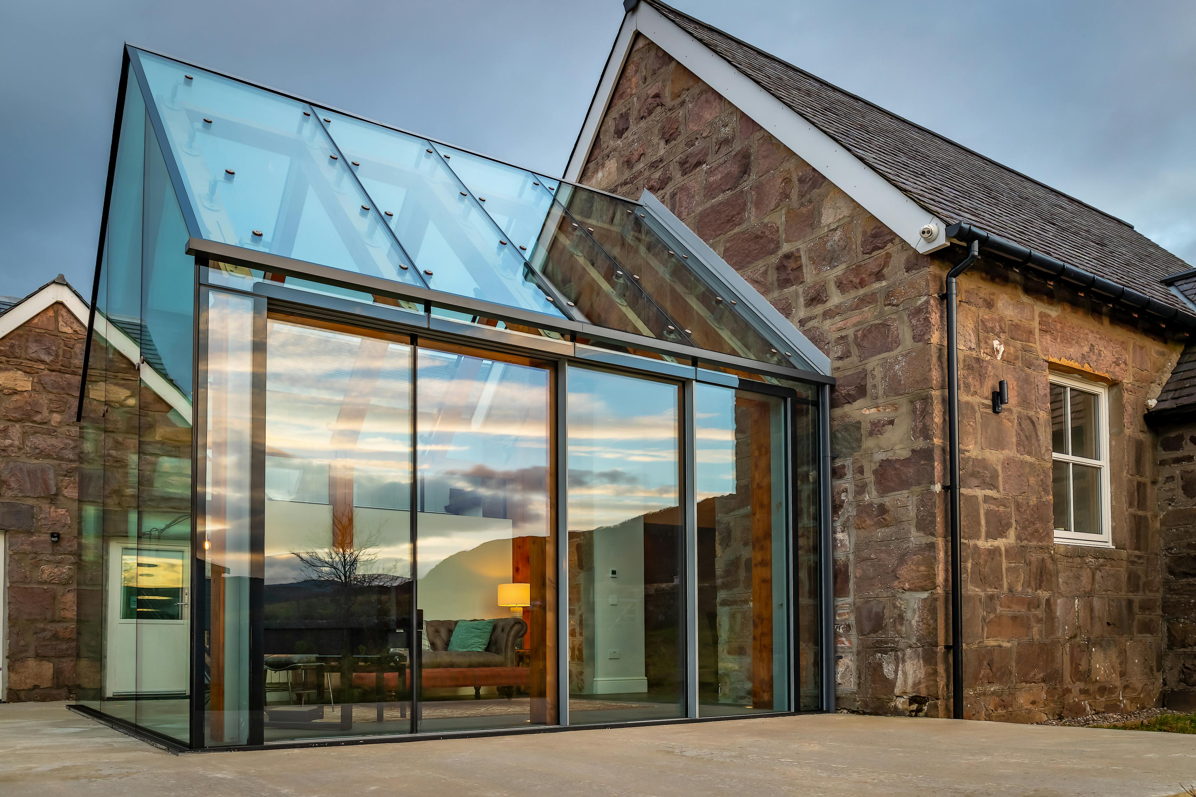 External view of a glazed extension attached to a stone cottage in Scotland, blending modern glass design with the rustic charm of the traditional stone structure