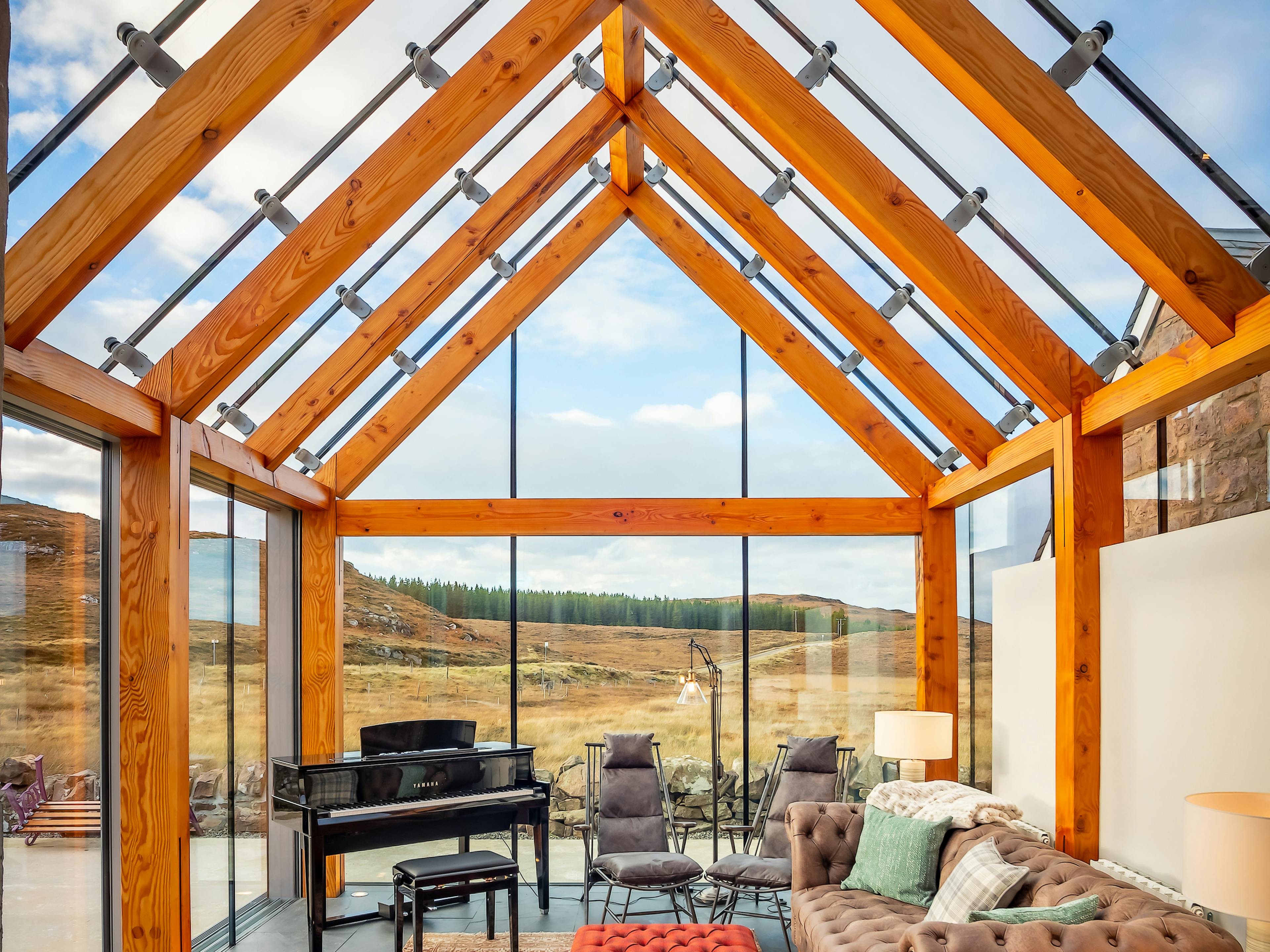 Internal view of a glazed extension featuring a timber-framed structure, seamlessly integrated with a stone cottage and offering stunning coastal views in Scotland