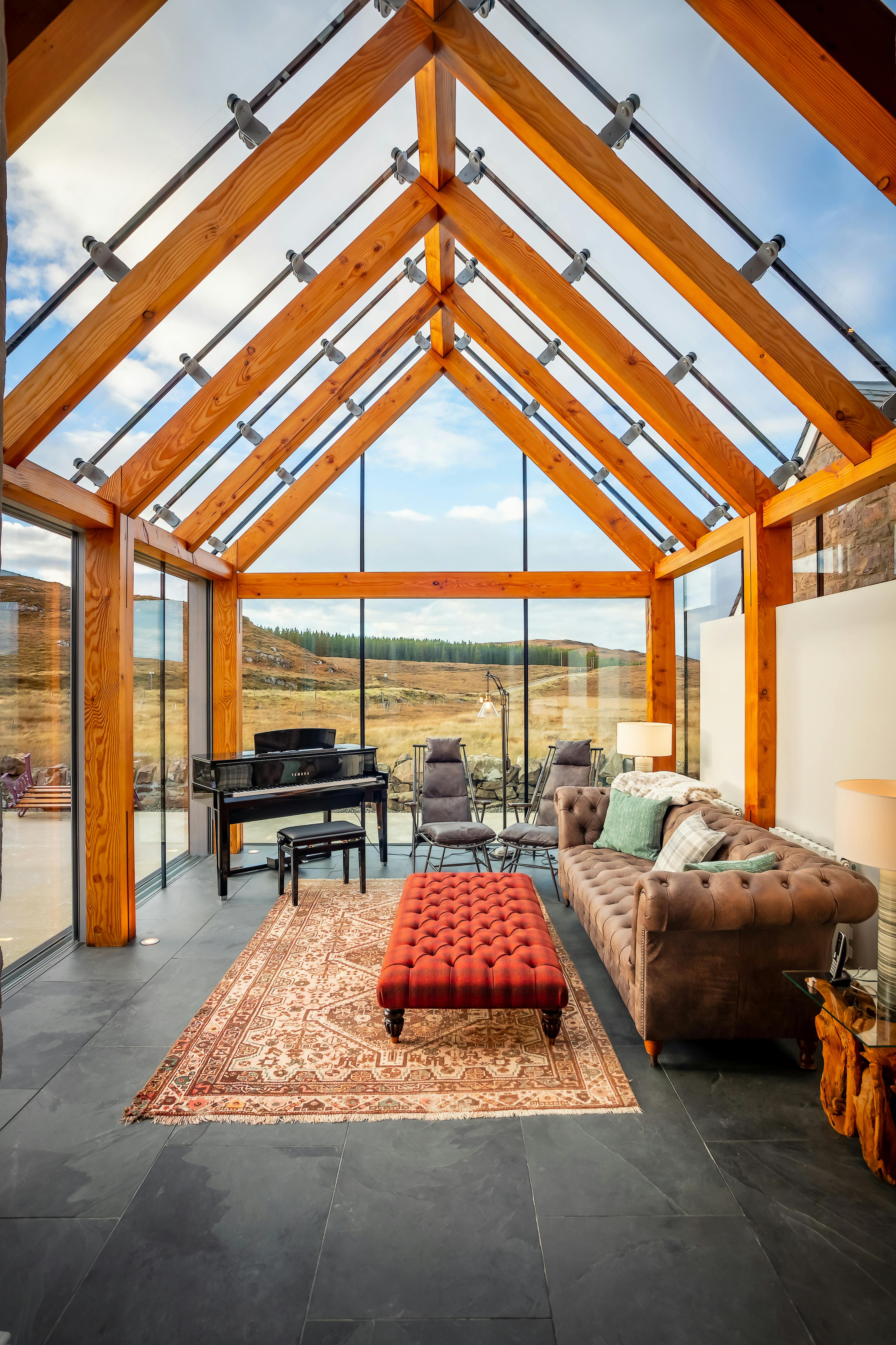 Internal view of a glazed extension featuring a timber-framed structure, seamlessly integrated with a stone cottage and offering stunning coastal views in Scotland