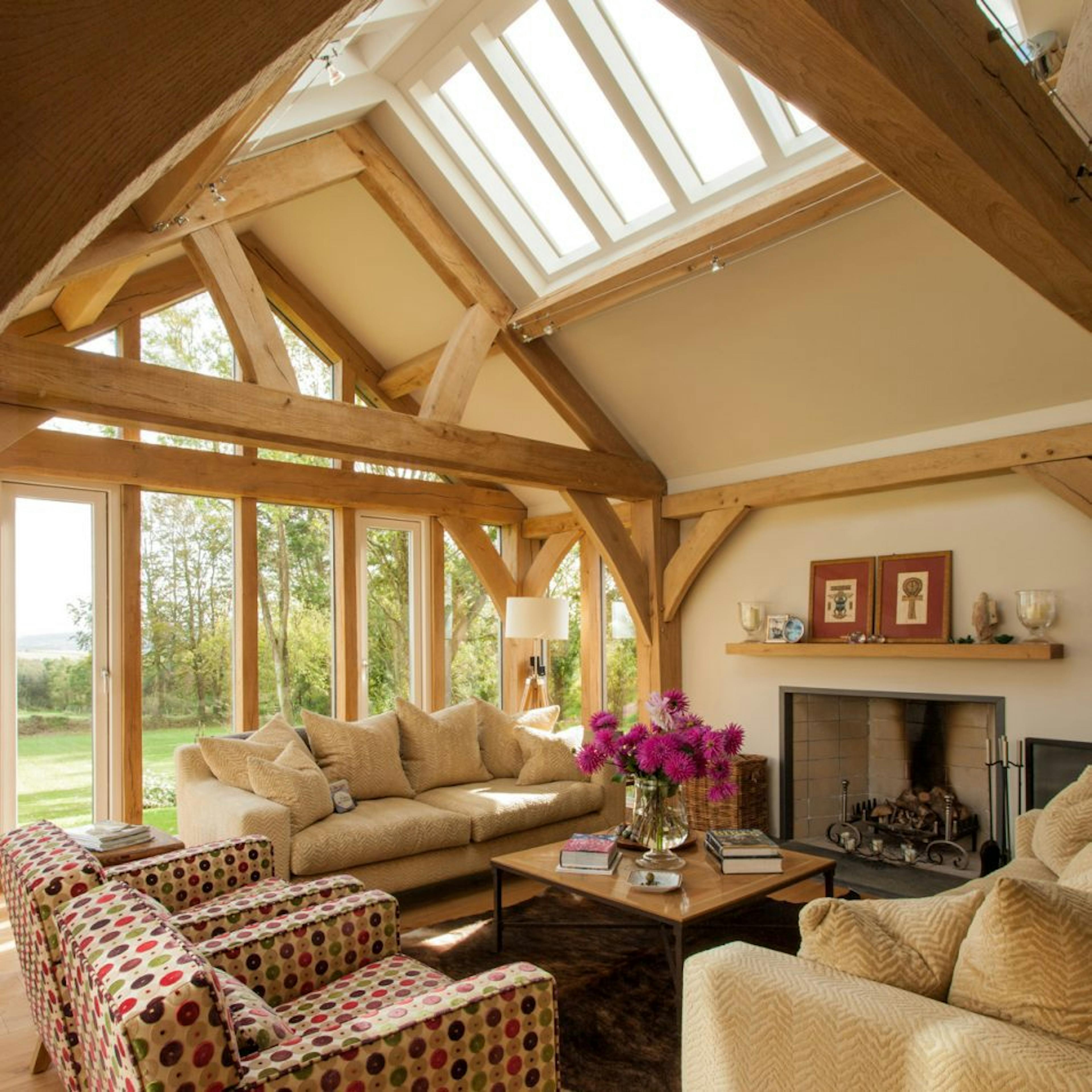 An oak-framed living space featuring queen posts and roof lanterns, allowing ample natural light to flood the area, along with a glazed gable end that enhances the bright, airy feel