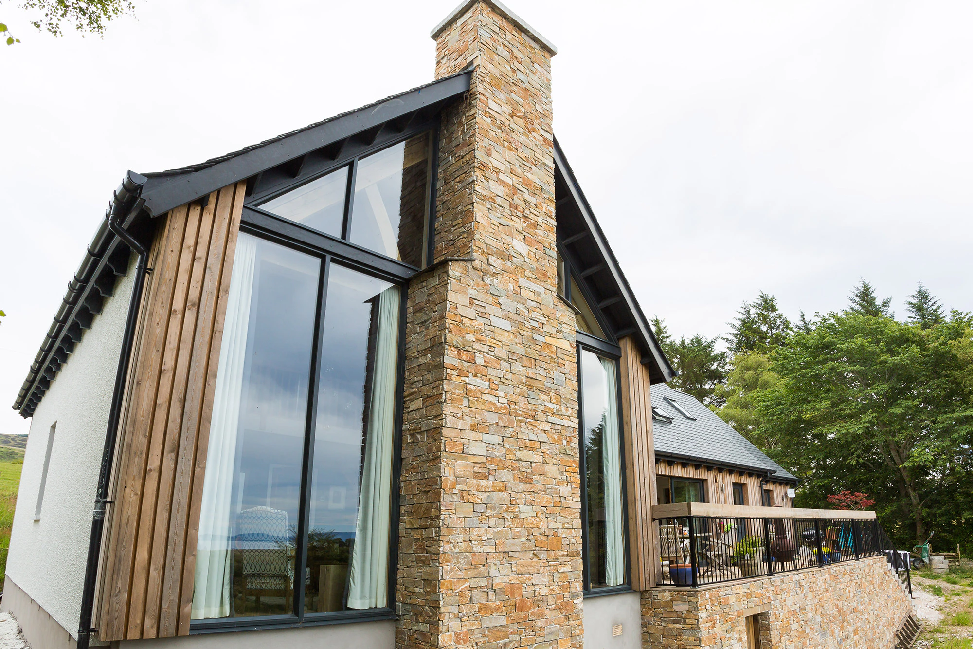 External view of an oak-framed family home featuring a vaulted living space and a central stone fireplace within a glazed gable end