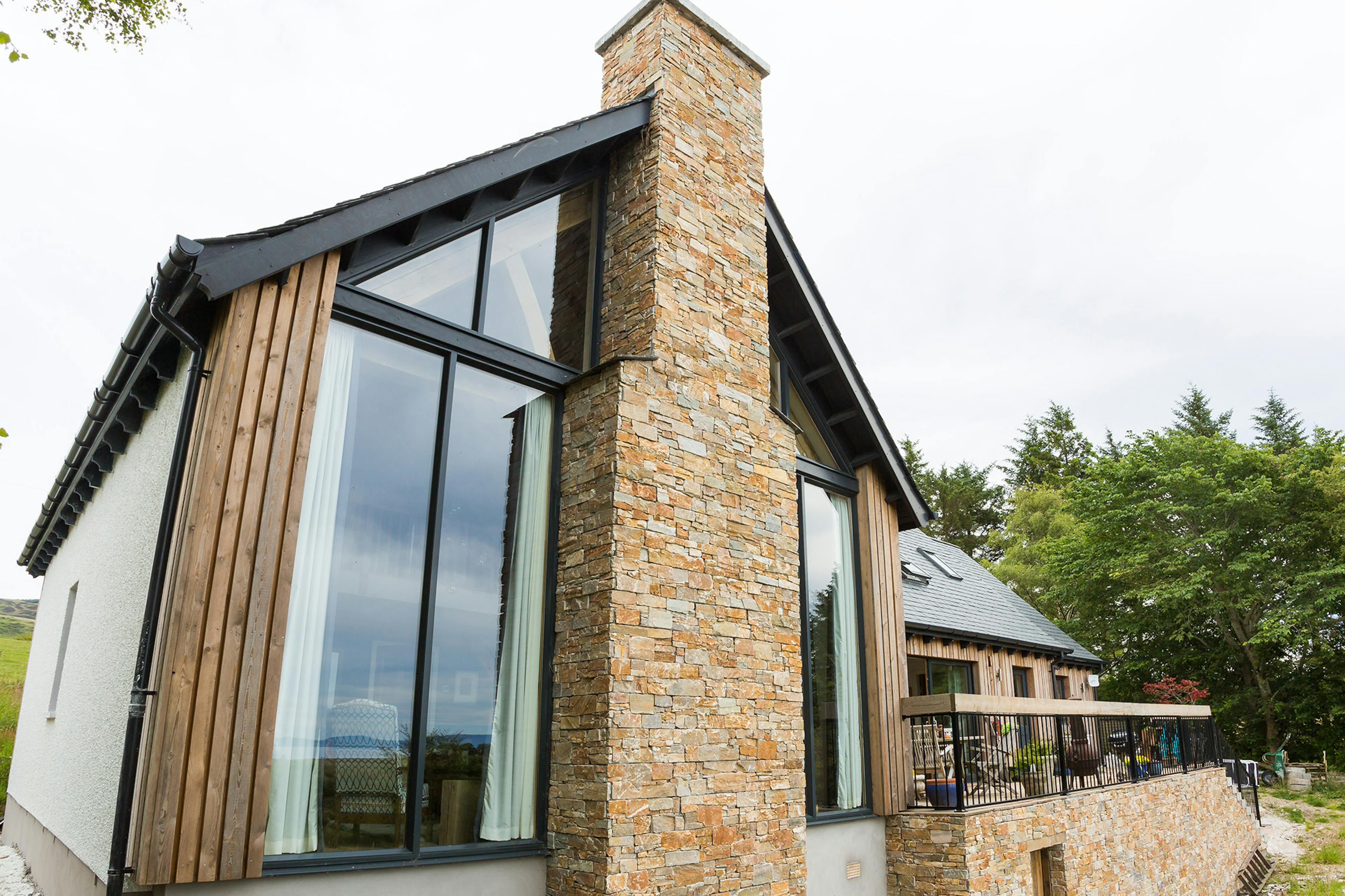 External view of an oak-framed family home featuring a vaulted living space and a central stone fireplace within a glazed gable end