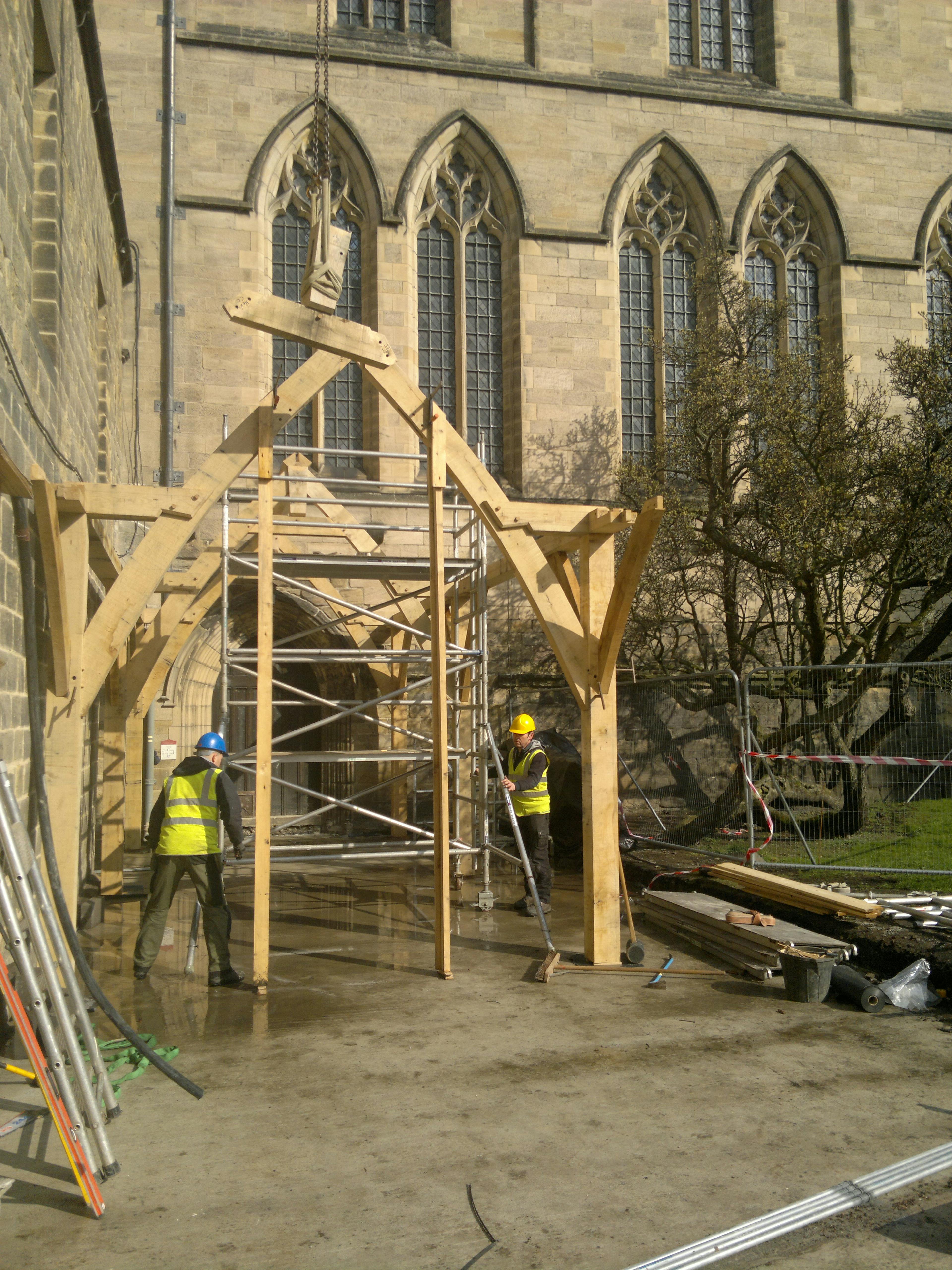 On-site assembly of the oak-framed cloister at Hexham Abbey featuring sling brace trusses, chamfered lapped dovetails, and a distinctive diamond-shaped ridge beam