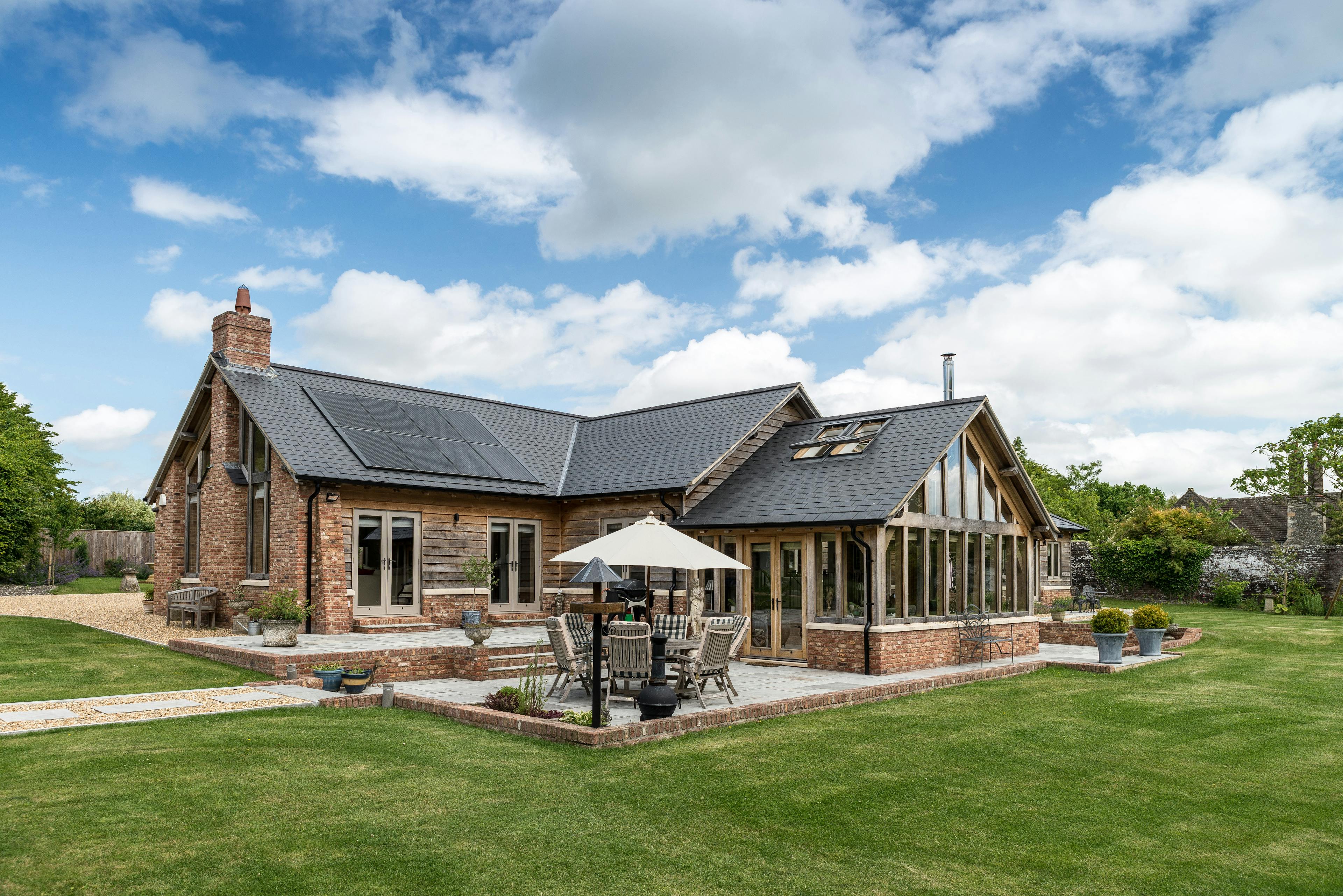 Green oak barn-style home surrounded by a spacious wraparound garden