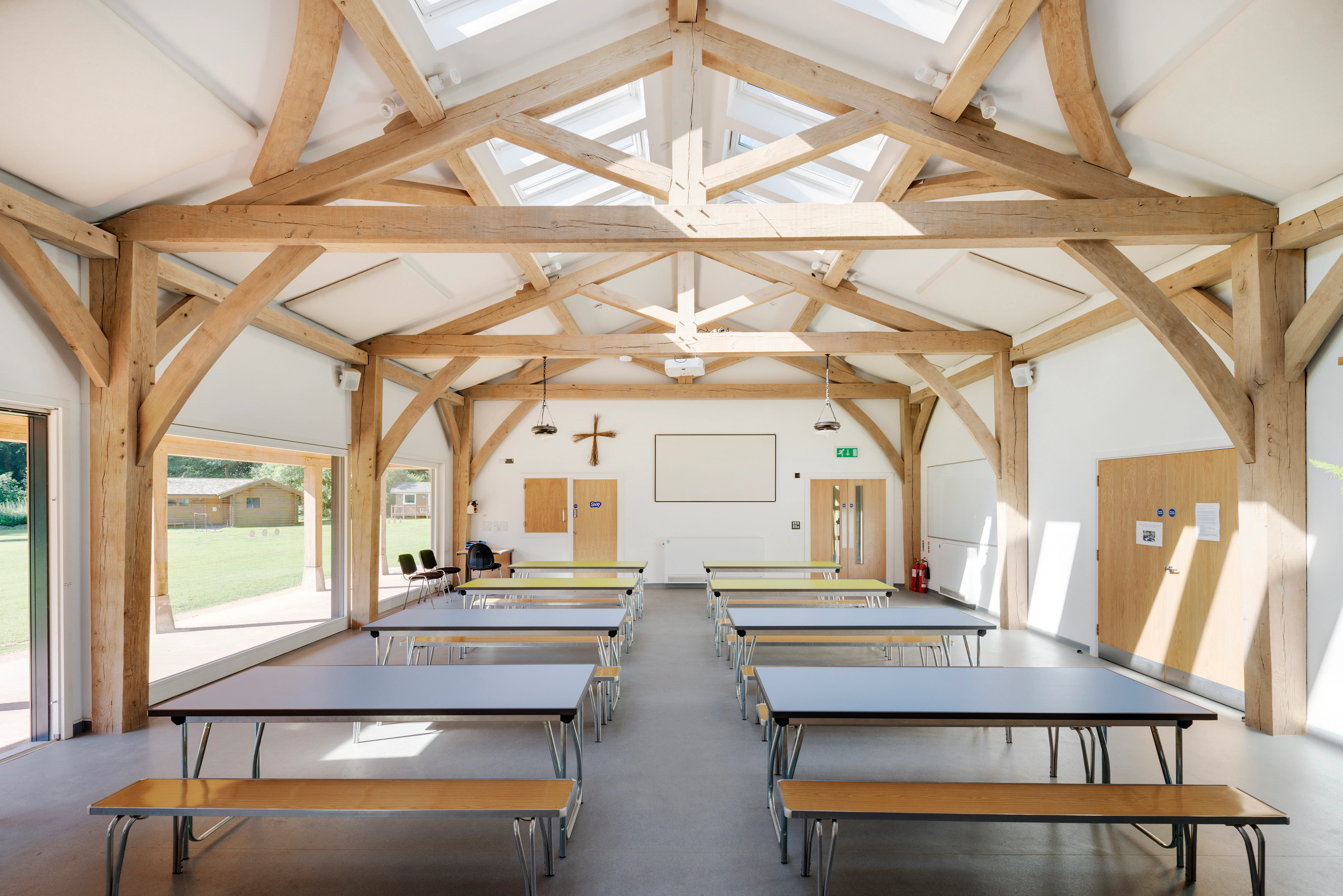 Interior view of the 4-bay multifunctional space at Great Wood Camp, featuring exposed kingpost trusses and roof lanterns that fill the space with natural light