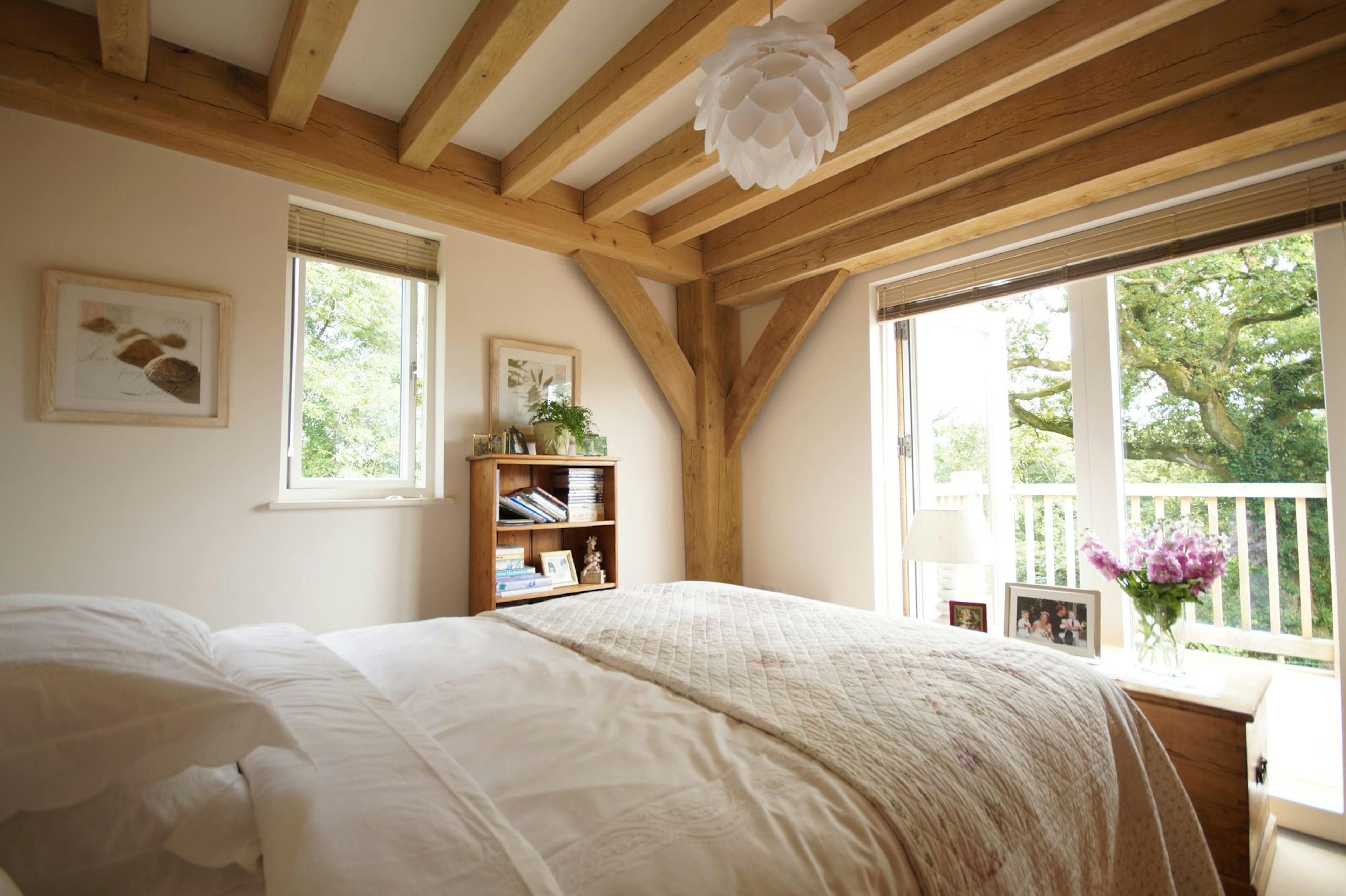 Oak-framed bedroom with double doors opening to a balcony offering views of the countryside