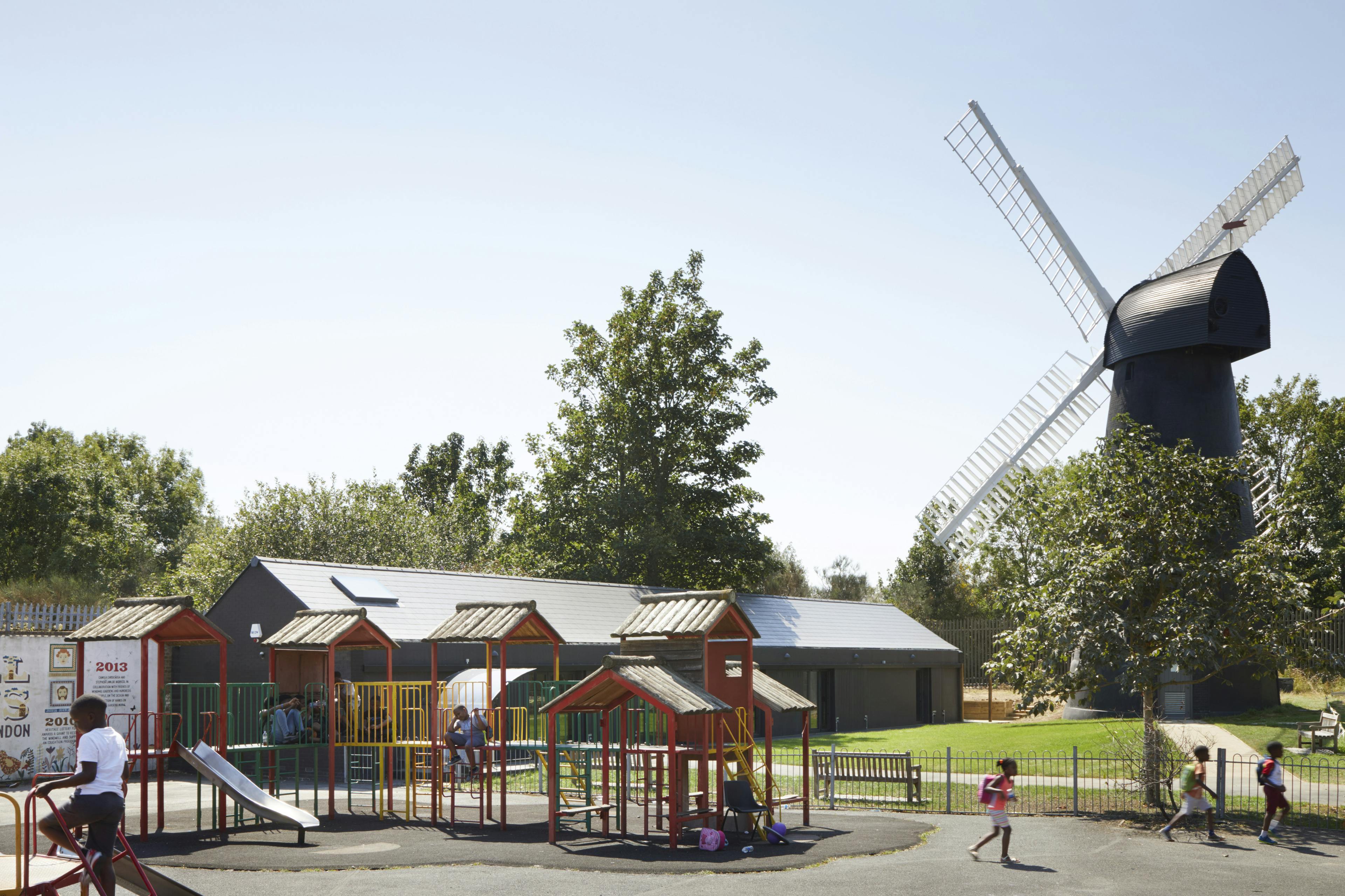 A playground by a black clad windmill and black clad timber framed community centre