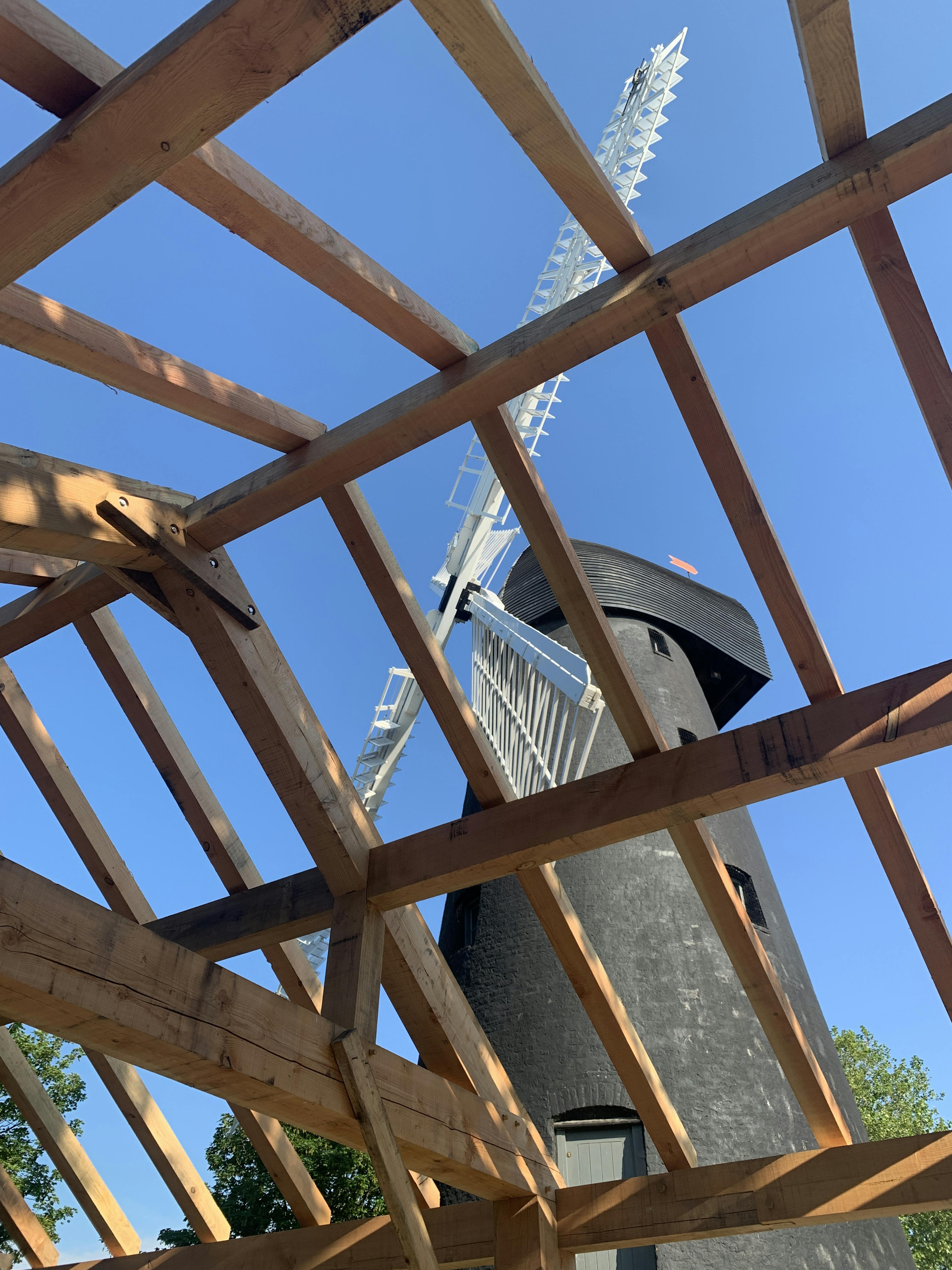 A Douglas fir framed community centre during construction with a black clad windmill viewable behind the frame