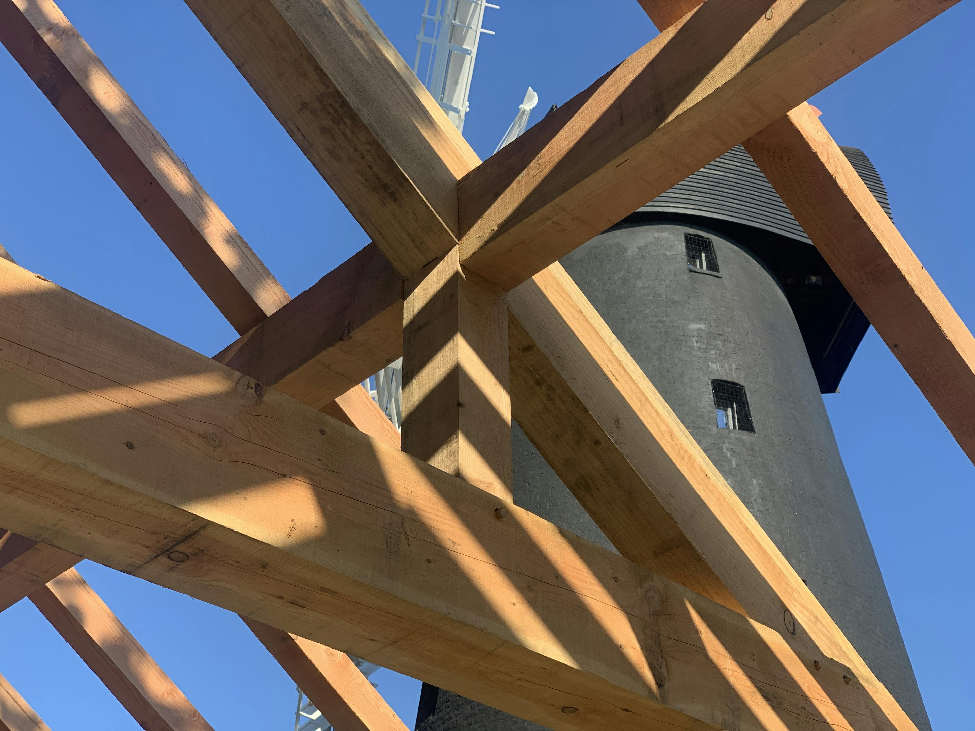 A Douglas fir framed community centre during construction with a black clad windmill viewable behind the frame