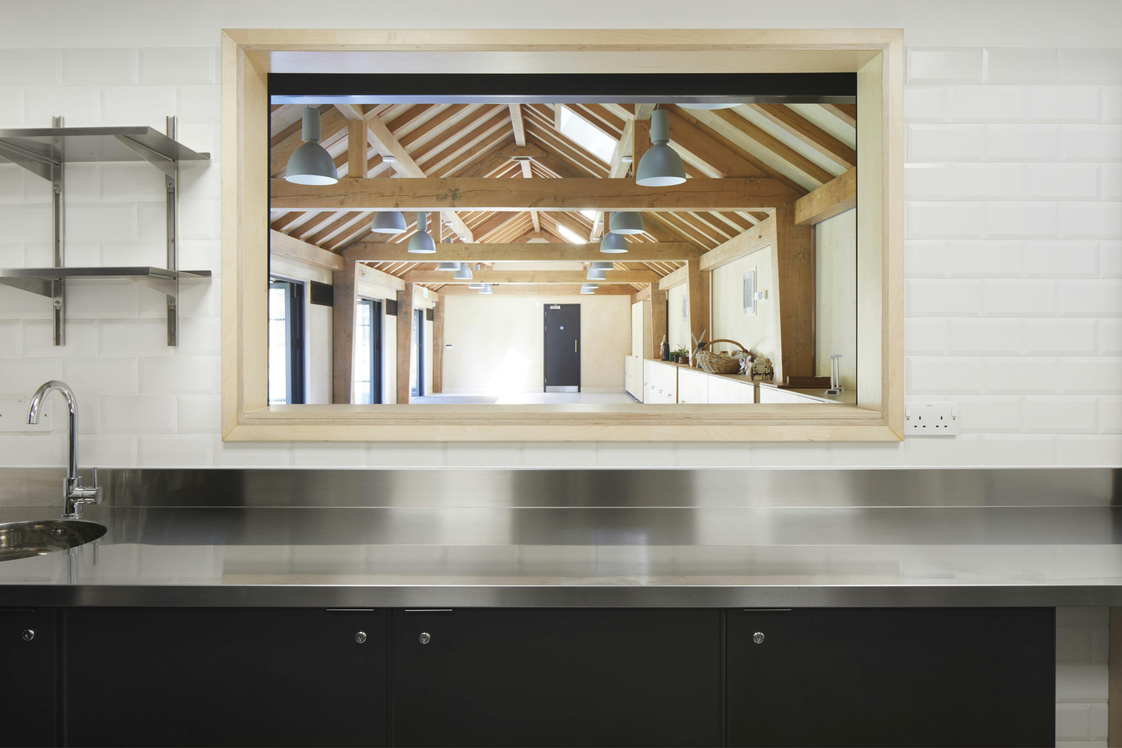 A Douglas fir framed community centre reflected in the mirror of a kitchen area