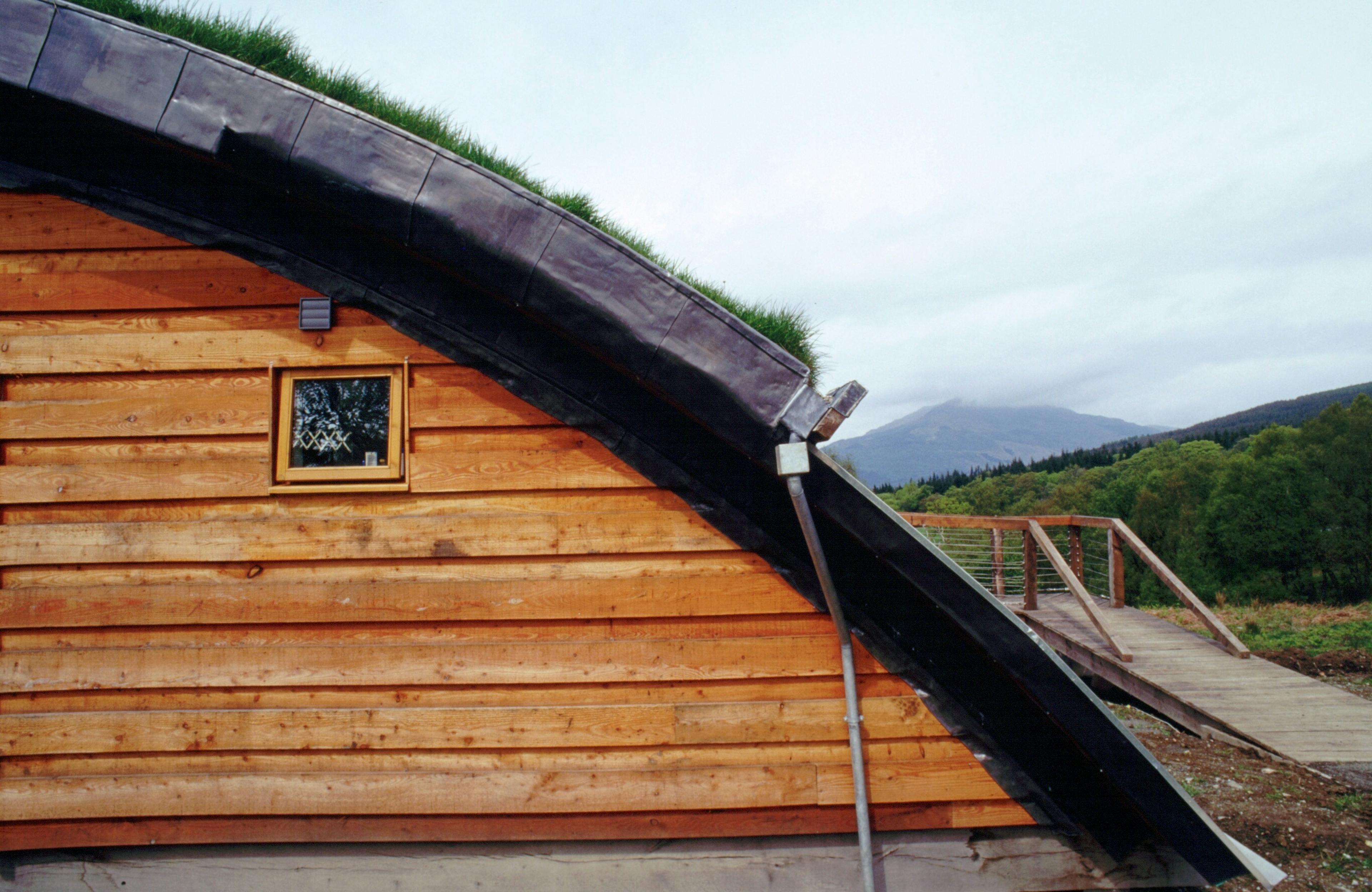 Close up of a green oak and Douglas fir clad cabin with a turfed curved roof
