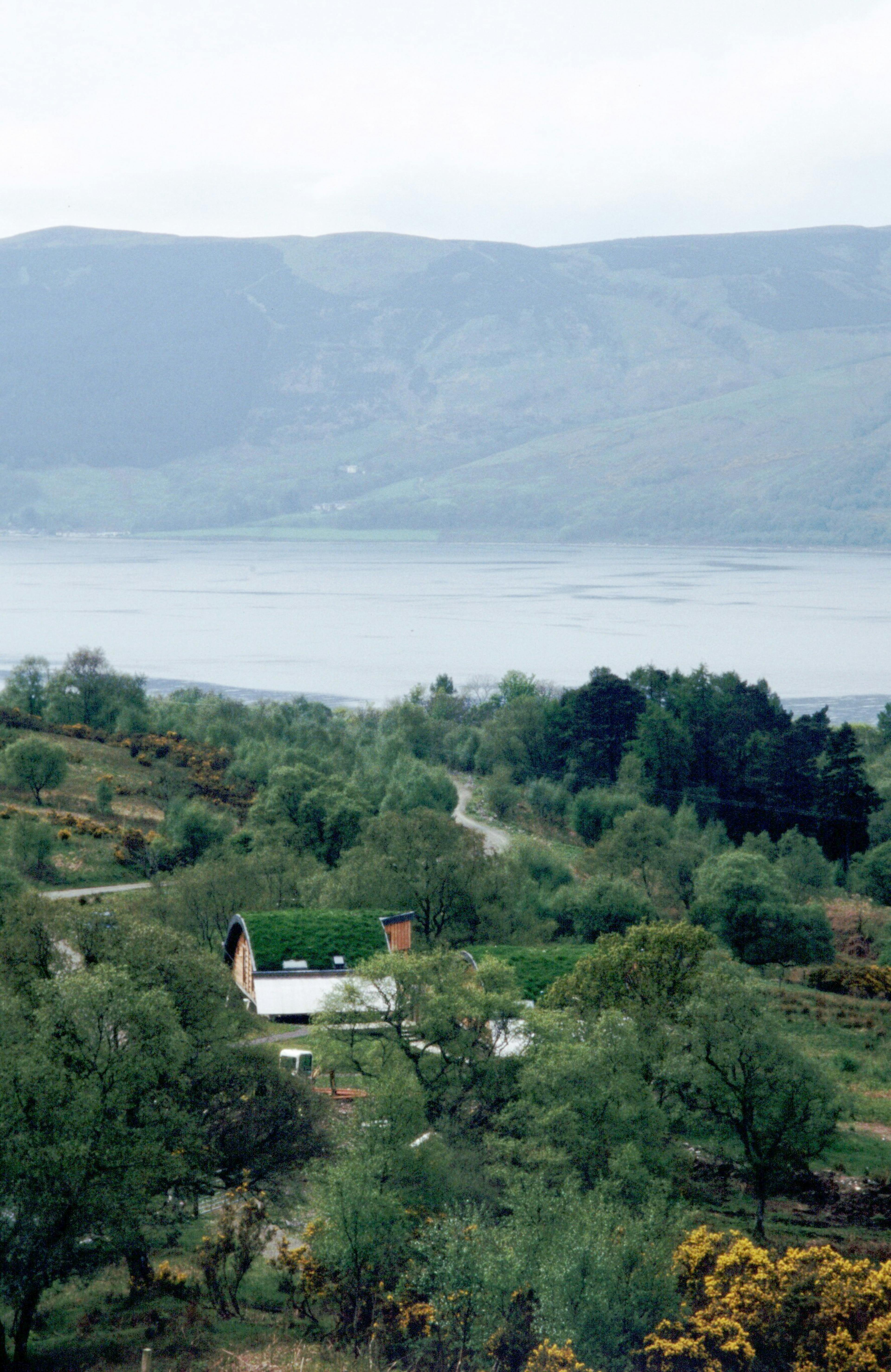 Green oak and Douglas fir clad cabins with a turfed curved roof in the distance
