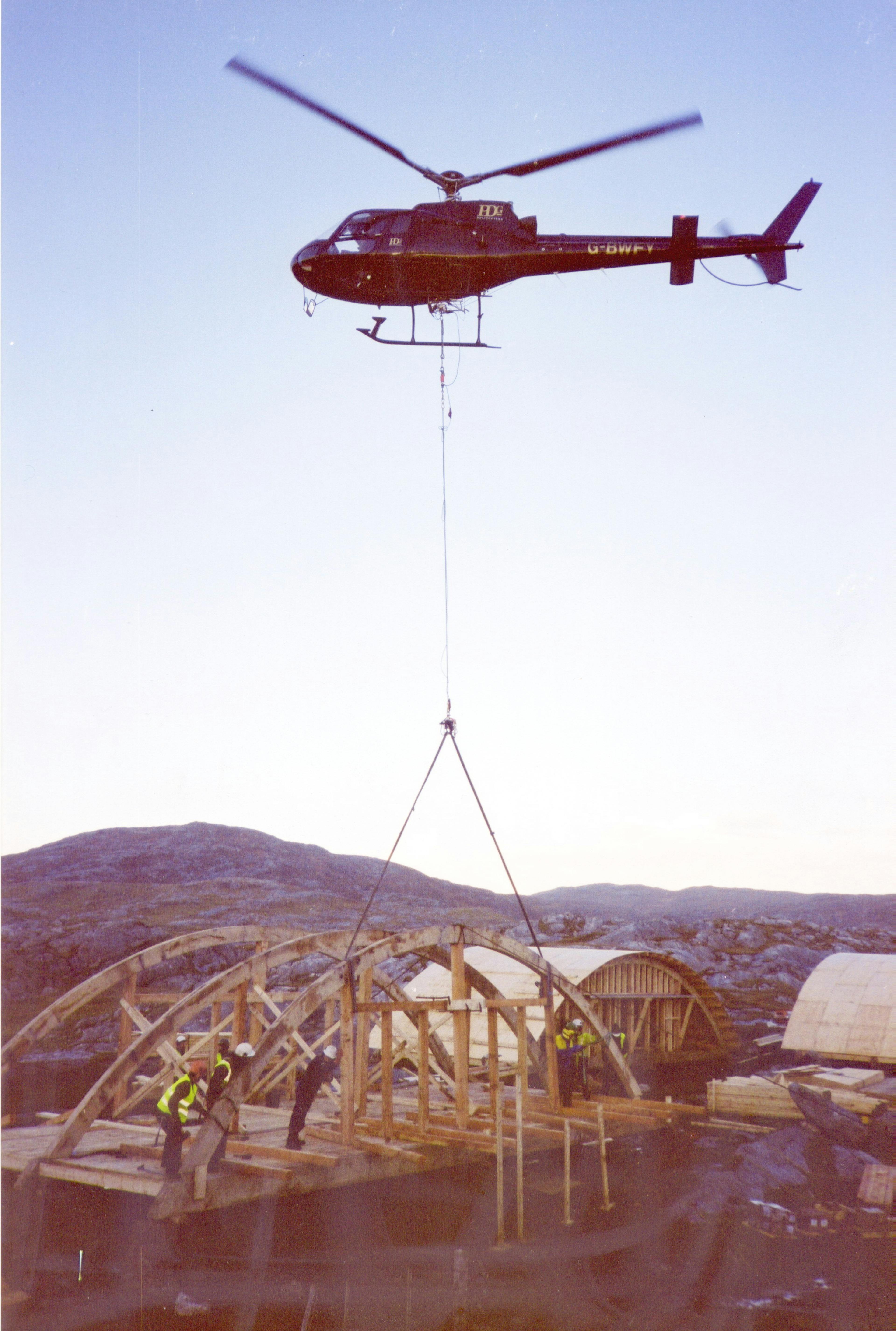 A helicopter landing a green oak frame for a cabin with a curved roof