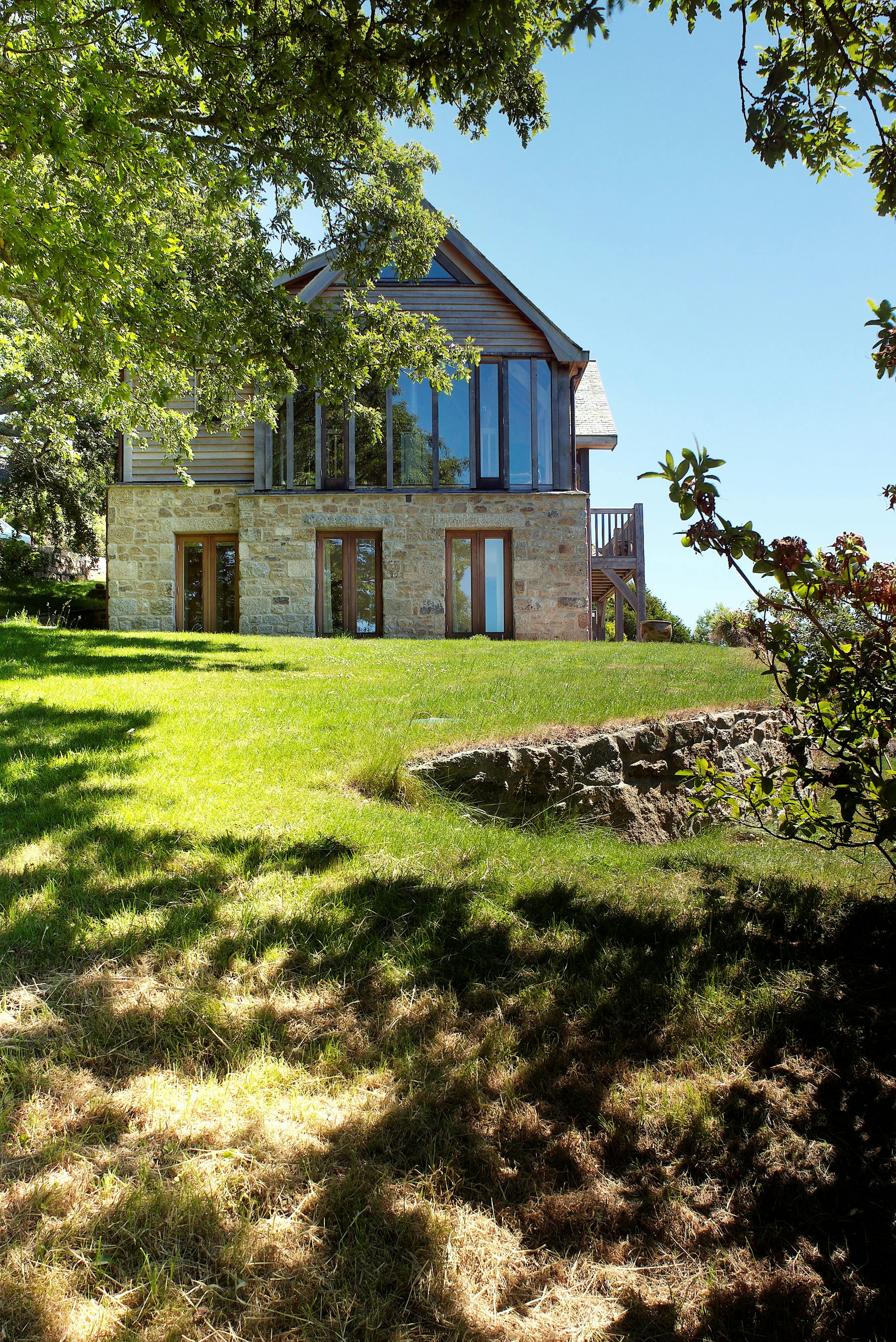 Oak frame home with stone cladding built on a slope with green lawn in front