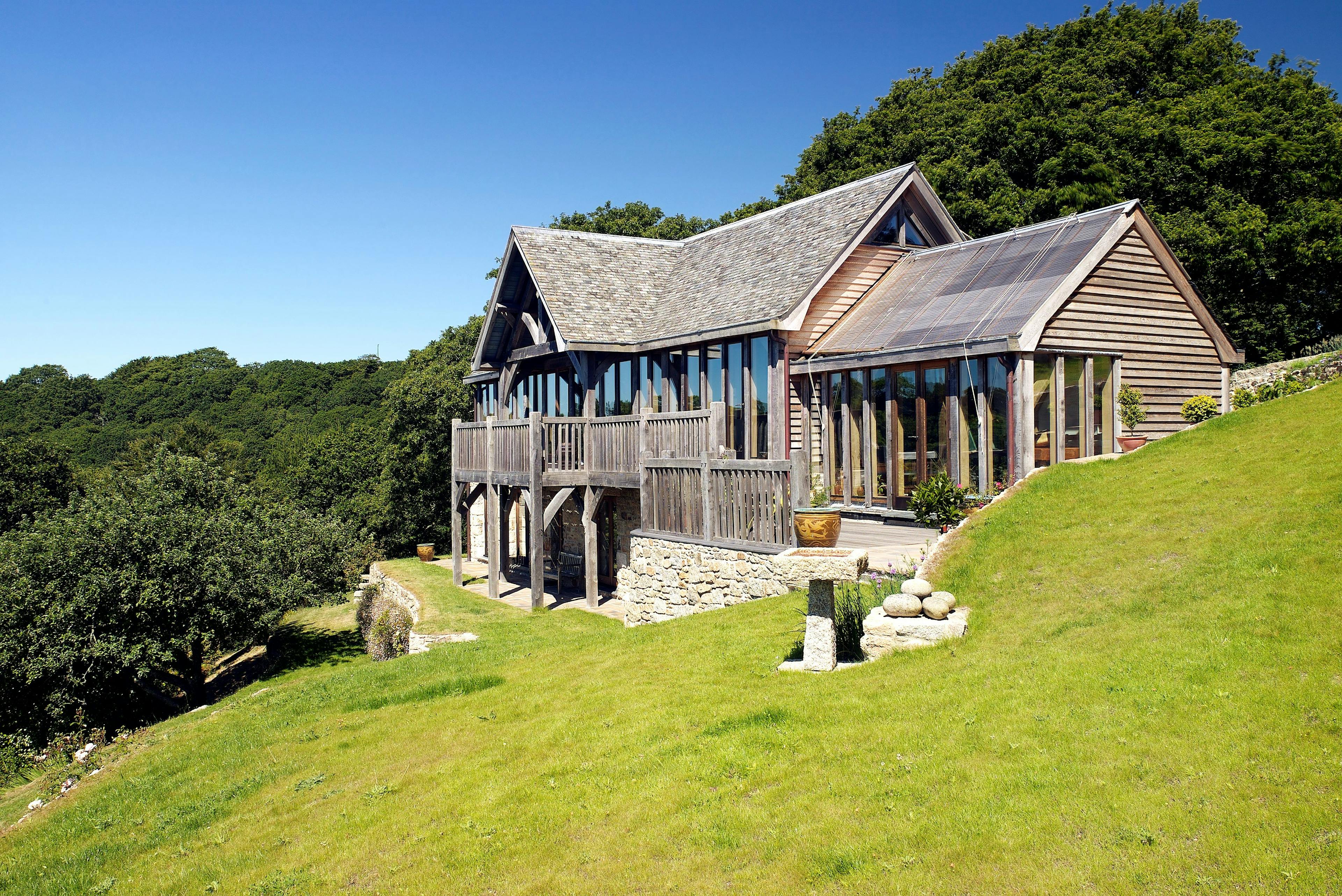 Oak frame home with oak balcony built on a slope with green lawn in front