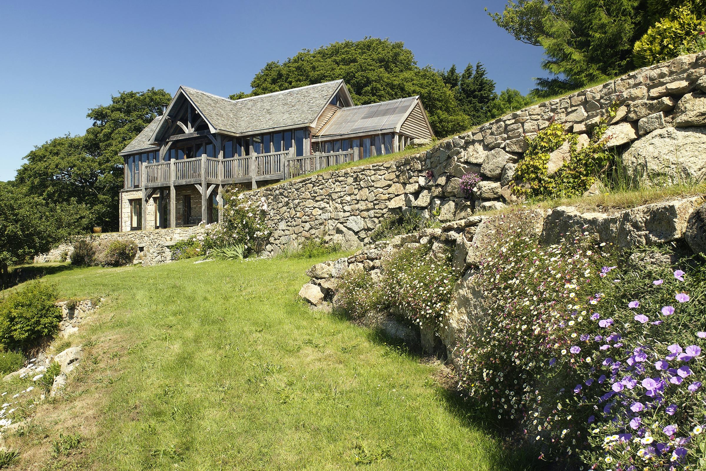Oak frame home with oak balcony built on a slope with green lawn in front