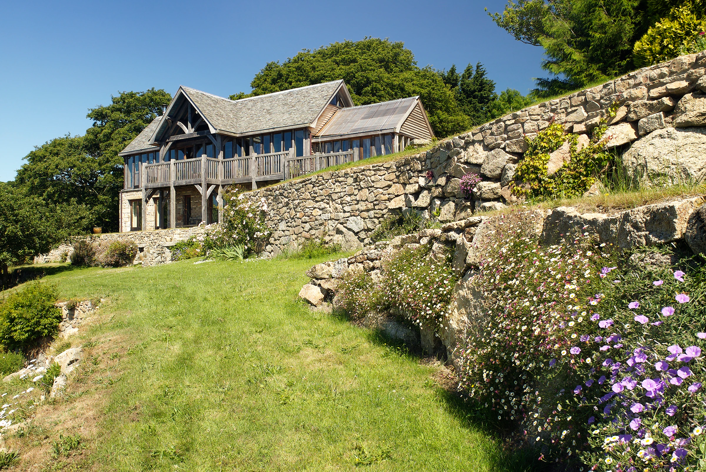 Oak frame home with oak balcony built on a slope with green lawn in front