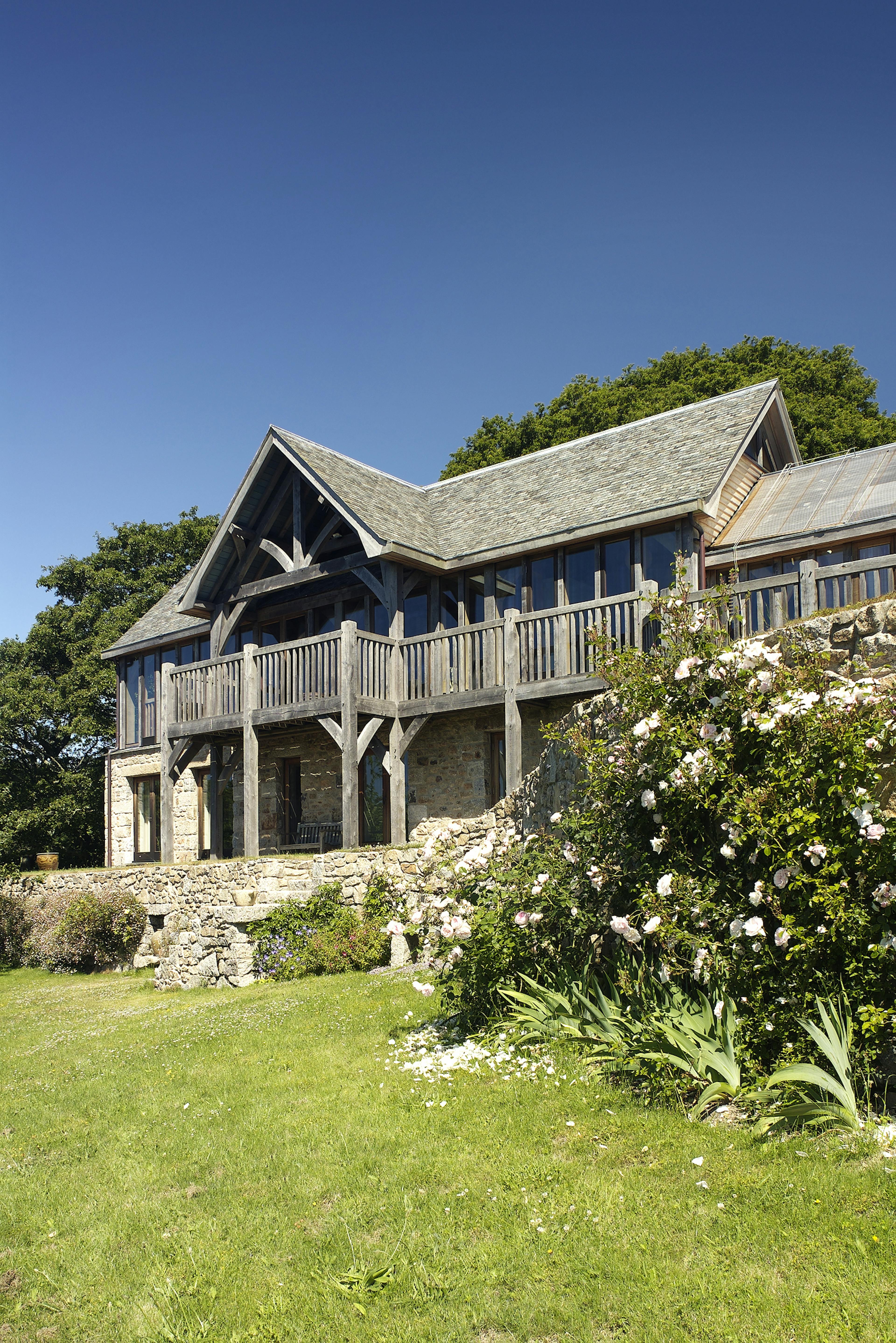 Oak frame home with oak balcony built on a slope with green lawn in front