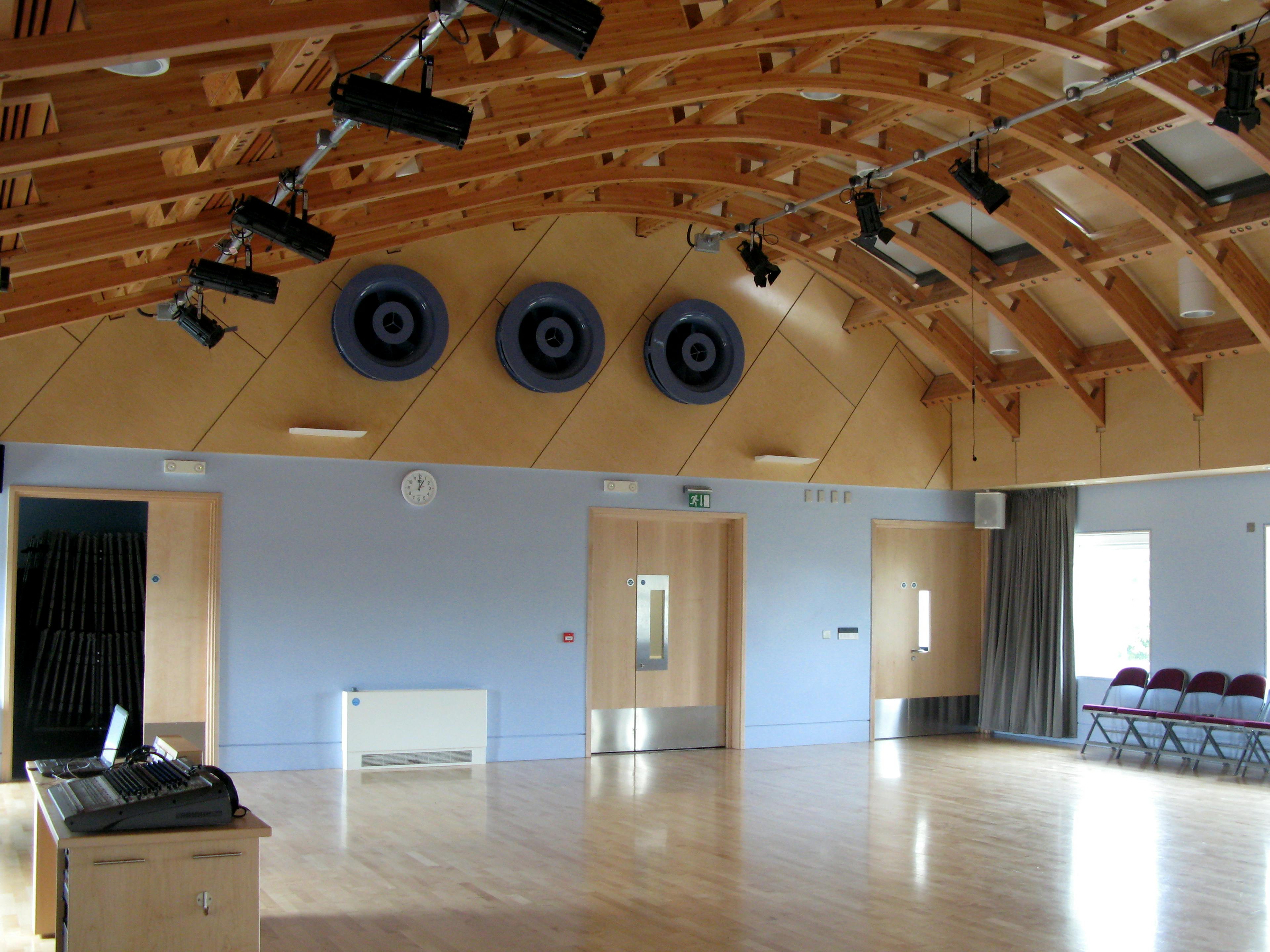 A hall with a glulam gridshell roof structure with a row of theatre lights