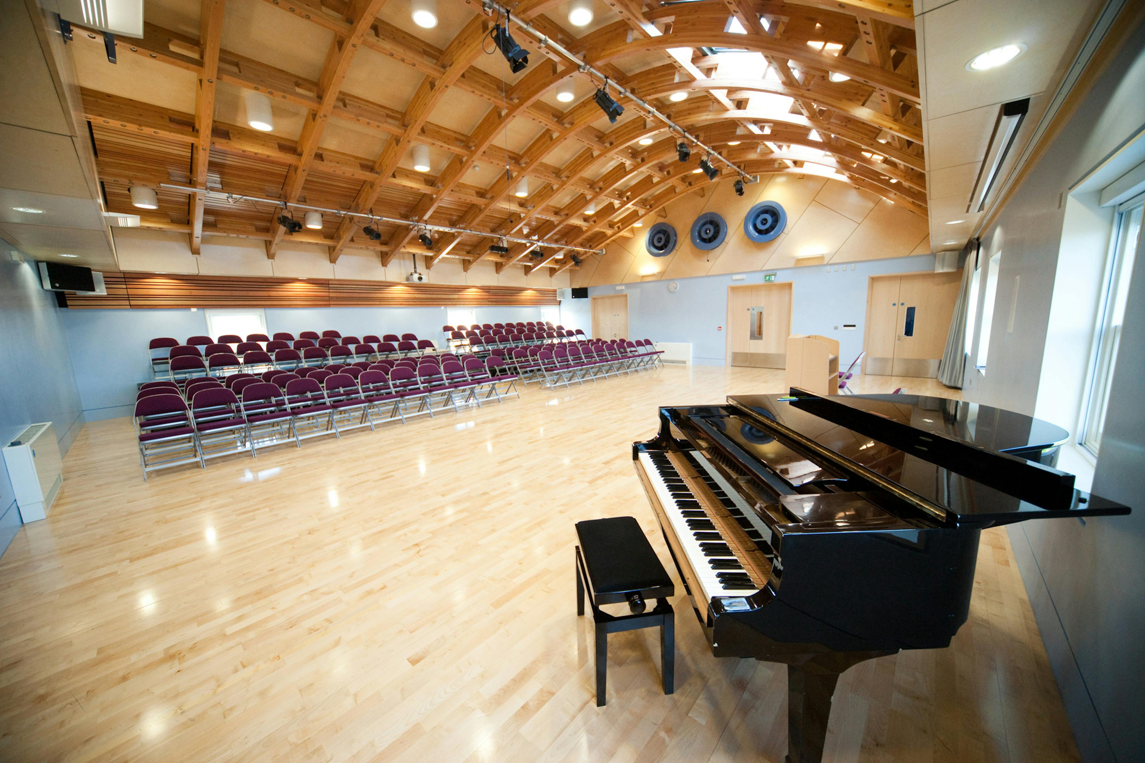 A hall with a glulam gridshell roof structure and rows of seating for an audience