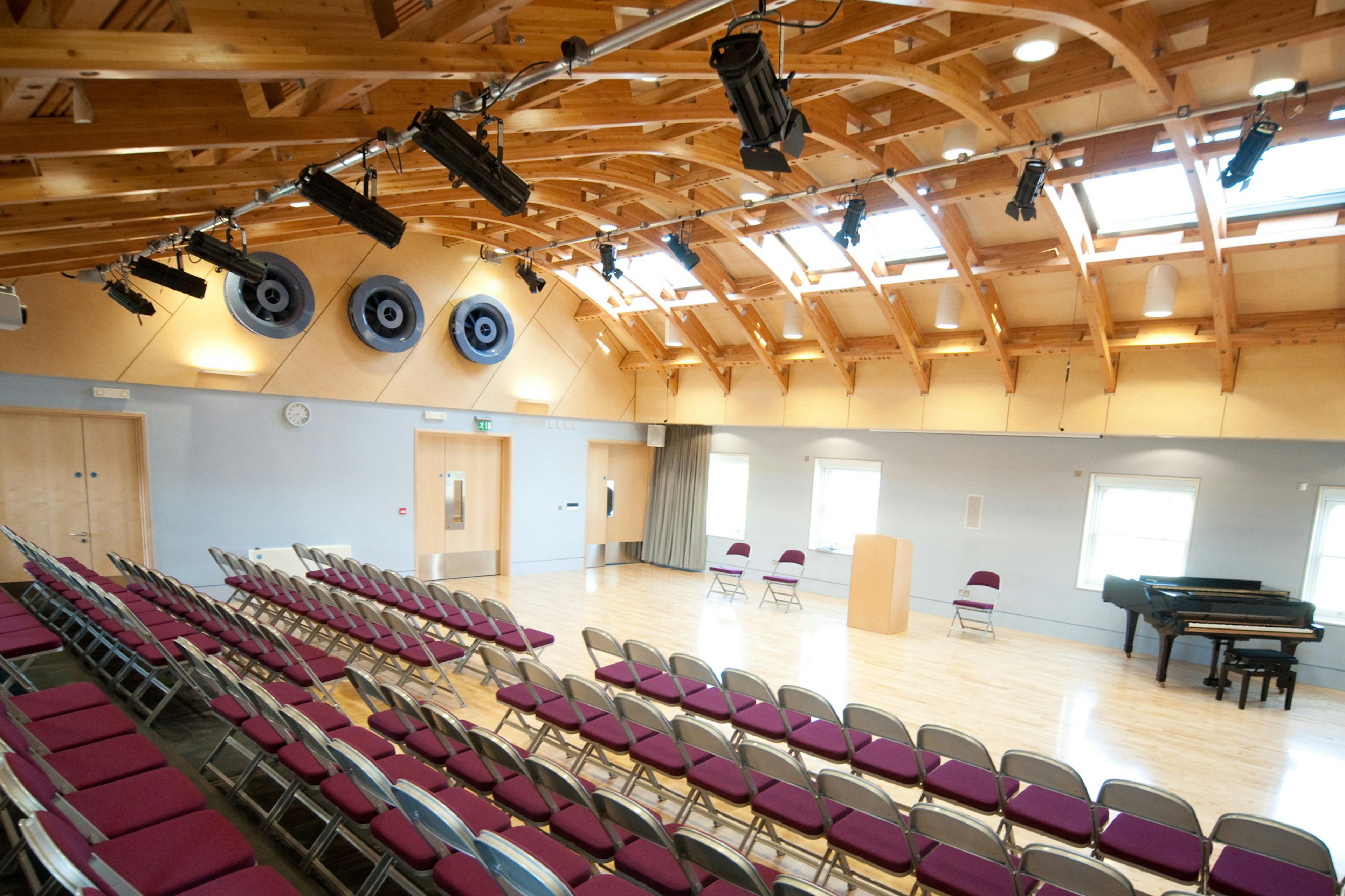 A hall with a glulam gridshell roof structure and rows of seating for an audience