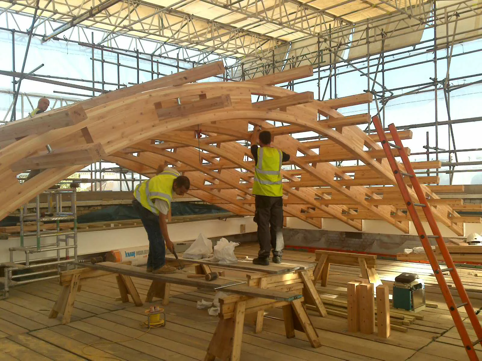 A glulam gridshell roof structure during installation with carpenters working on it