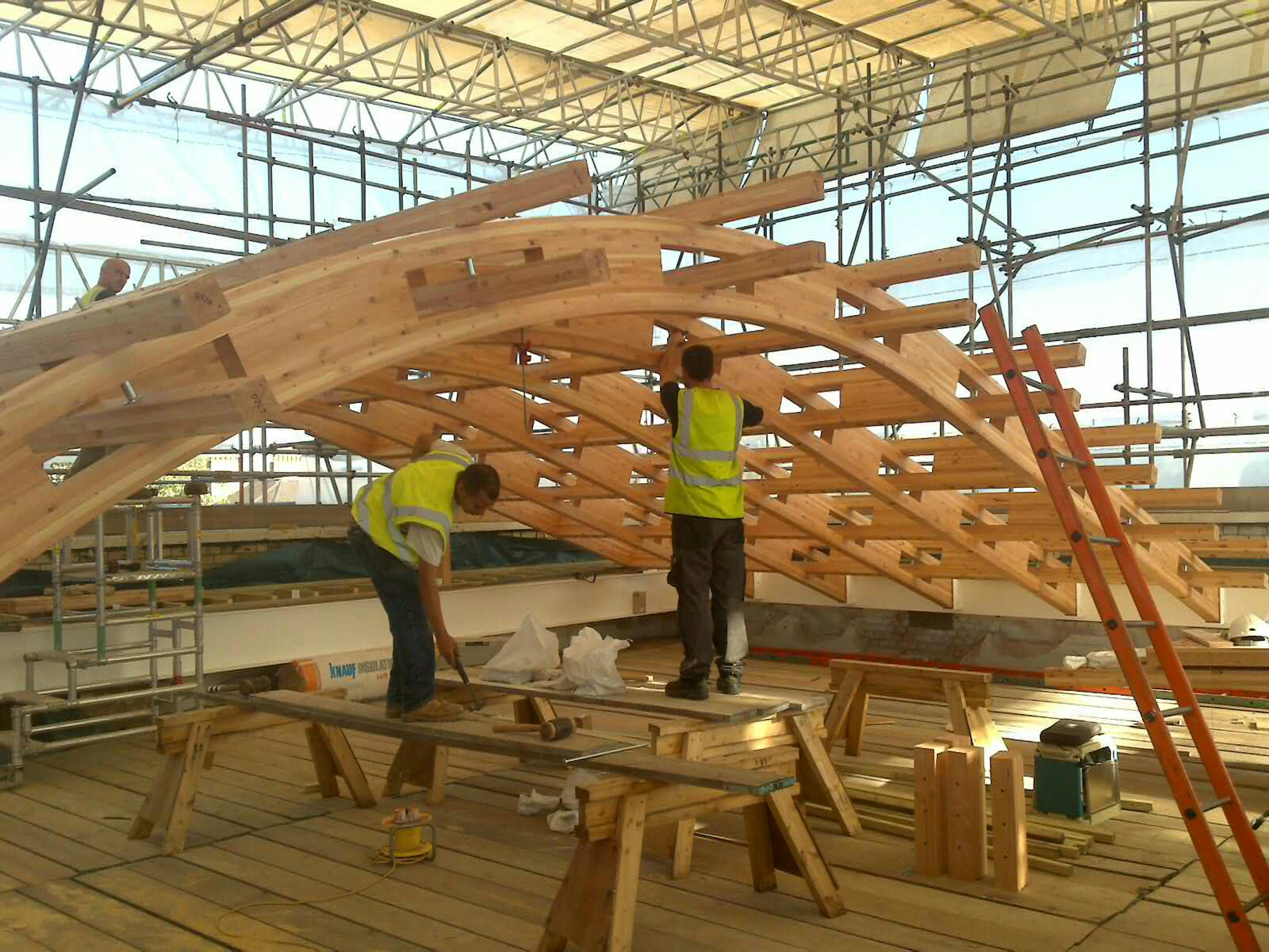 A glulam gridshell roof structure during installation with carpenters working on it