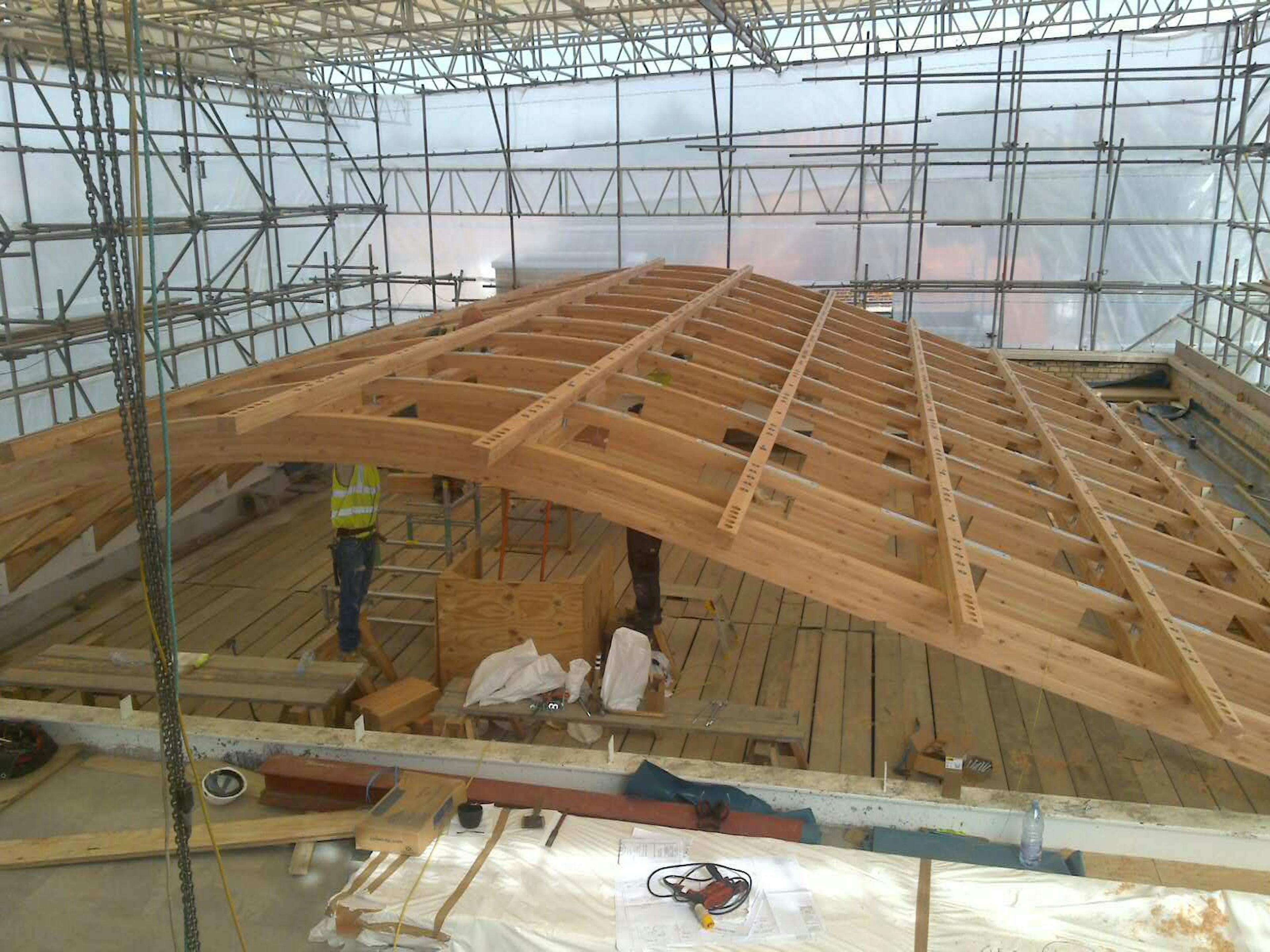 A glulam gridshell roof structure during installation with carpenters working on it