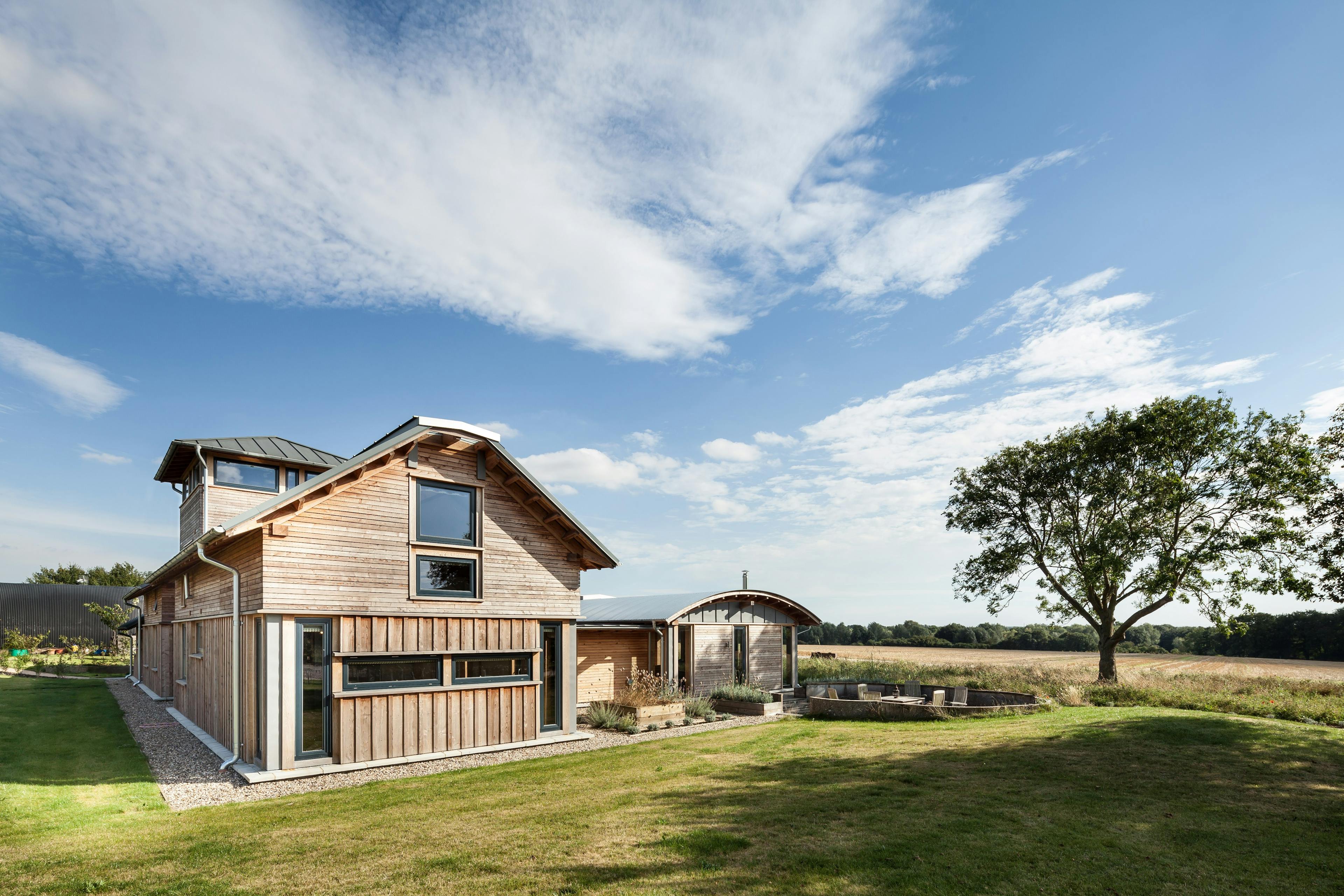 A side view of a timber clad large family farmhouse with a tower surrounded by a green lawn