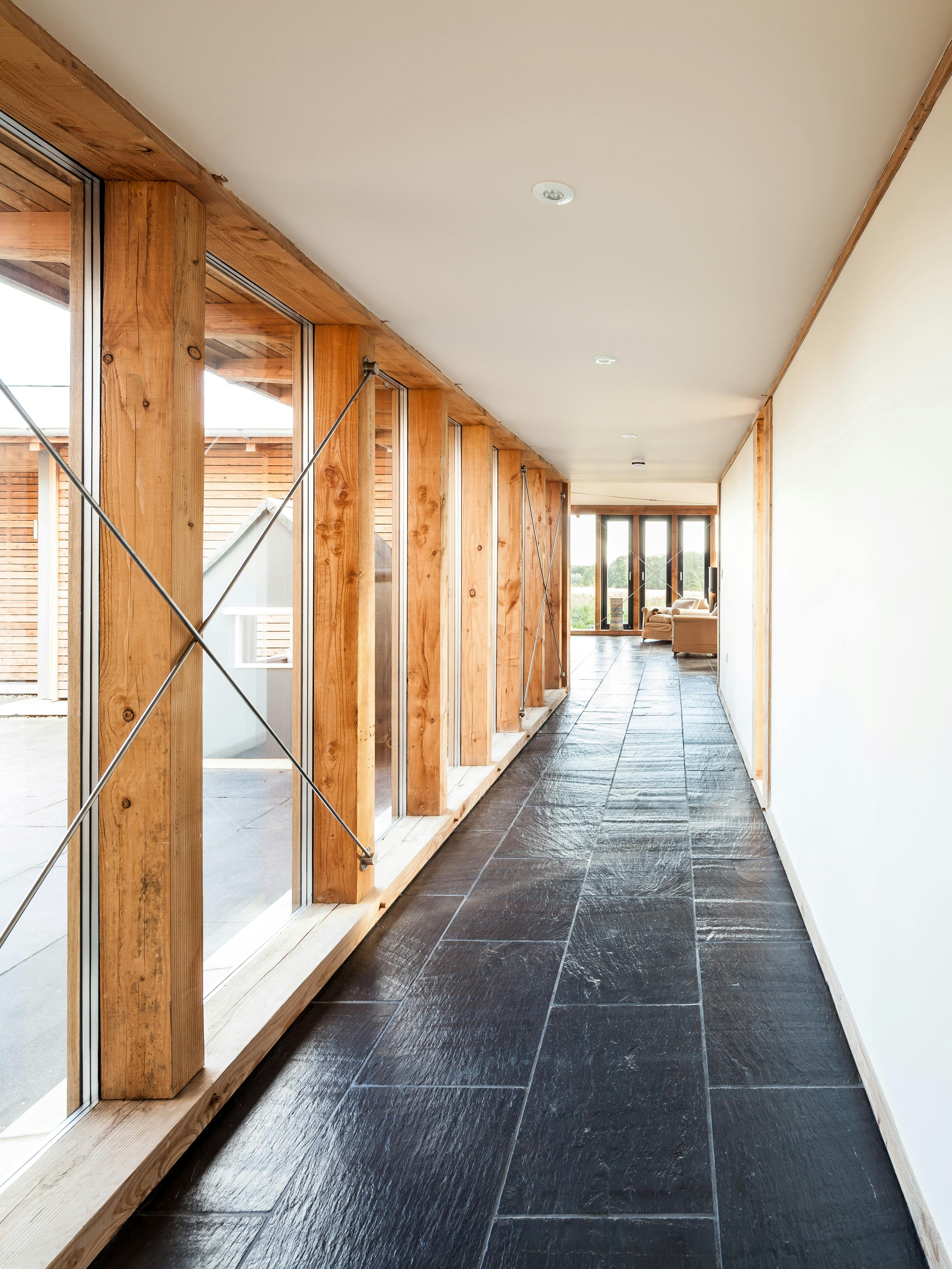 A glazed corridor in a Douglas fir framed family farmhouse with large dark grey flagstones on the floor