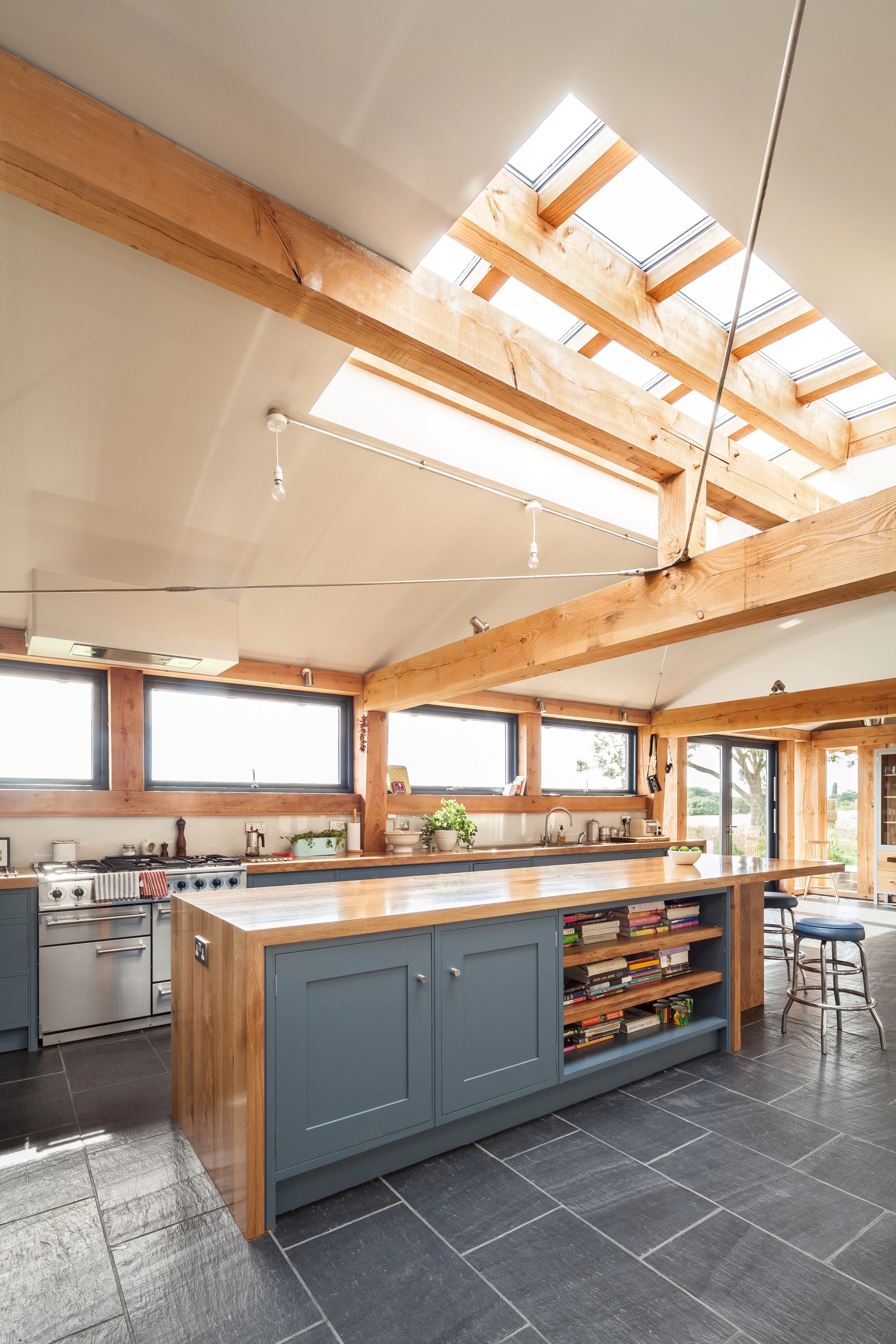 The kitchen in a Douglas fir framed family farmhouse with large dark grey flagstones on the floor and blue grey kitchen cabinets, and a roof lantern