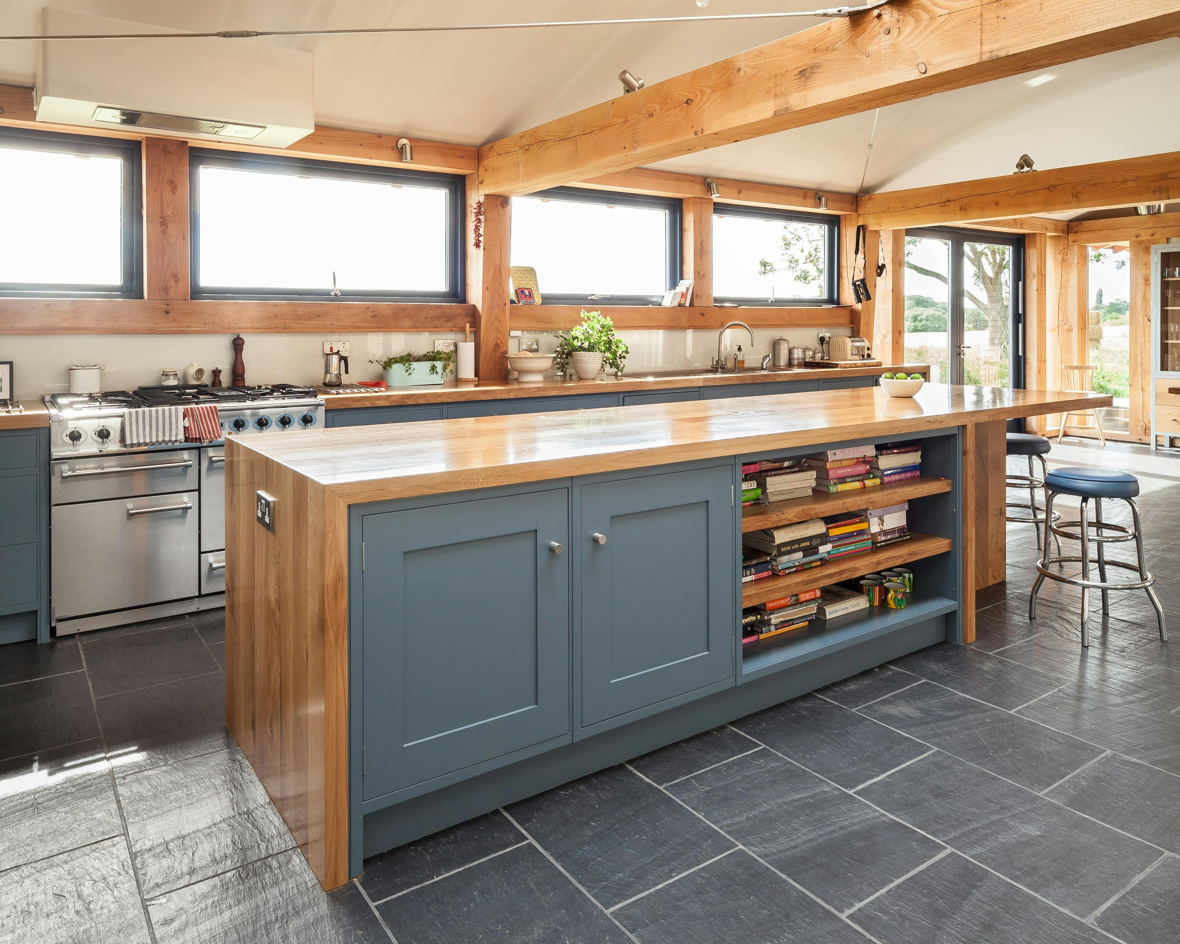 The kitchen in a Douglas fir framed family farmhouse with large dark grey flagstones on the floor and blue grey kitchen cabinets, and a roof lantern