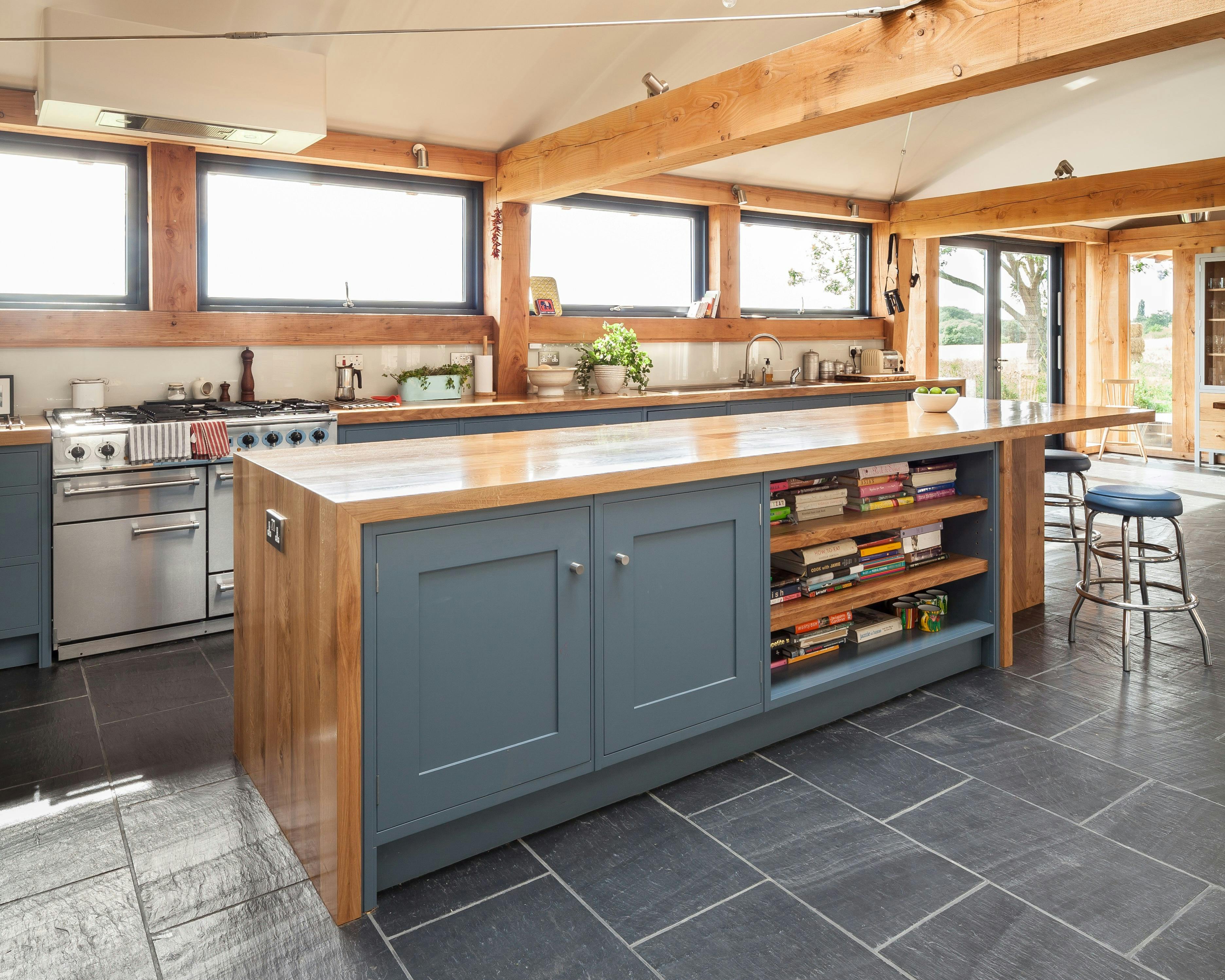 The kitchen in a Douglas fir framed family farmhouse with large dark grey flagstones on the floor and blue grey kitchen cabinets, and a roof lantern