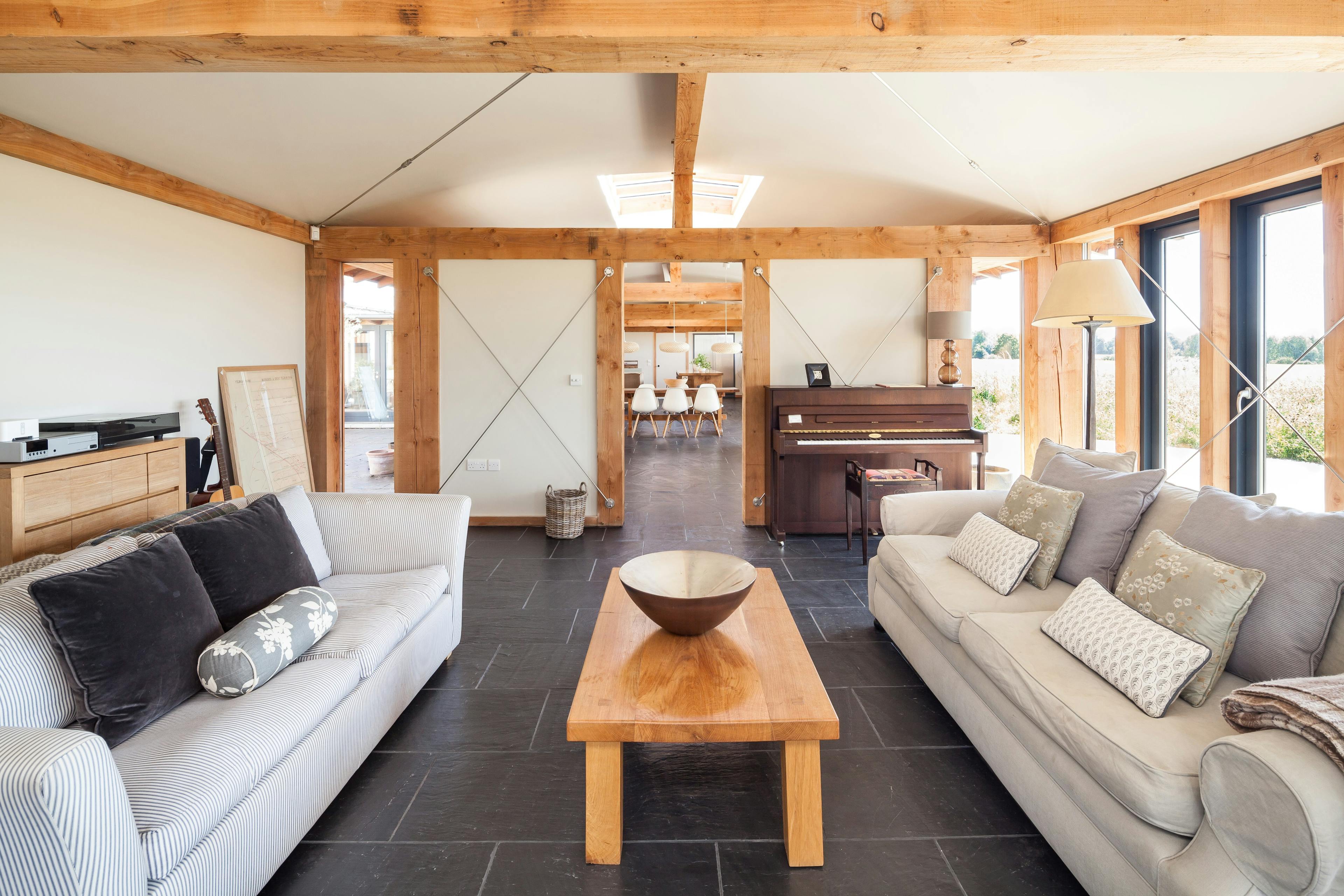 The sitting area in a Douglas fir framed family farmhouse with sofas and a piano and large glazing with views of the garden