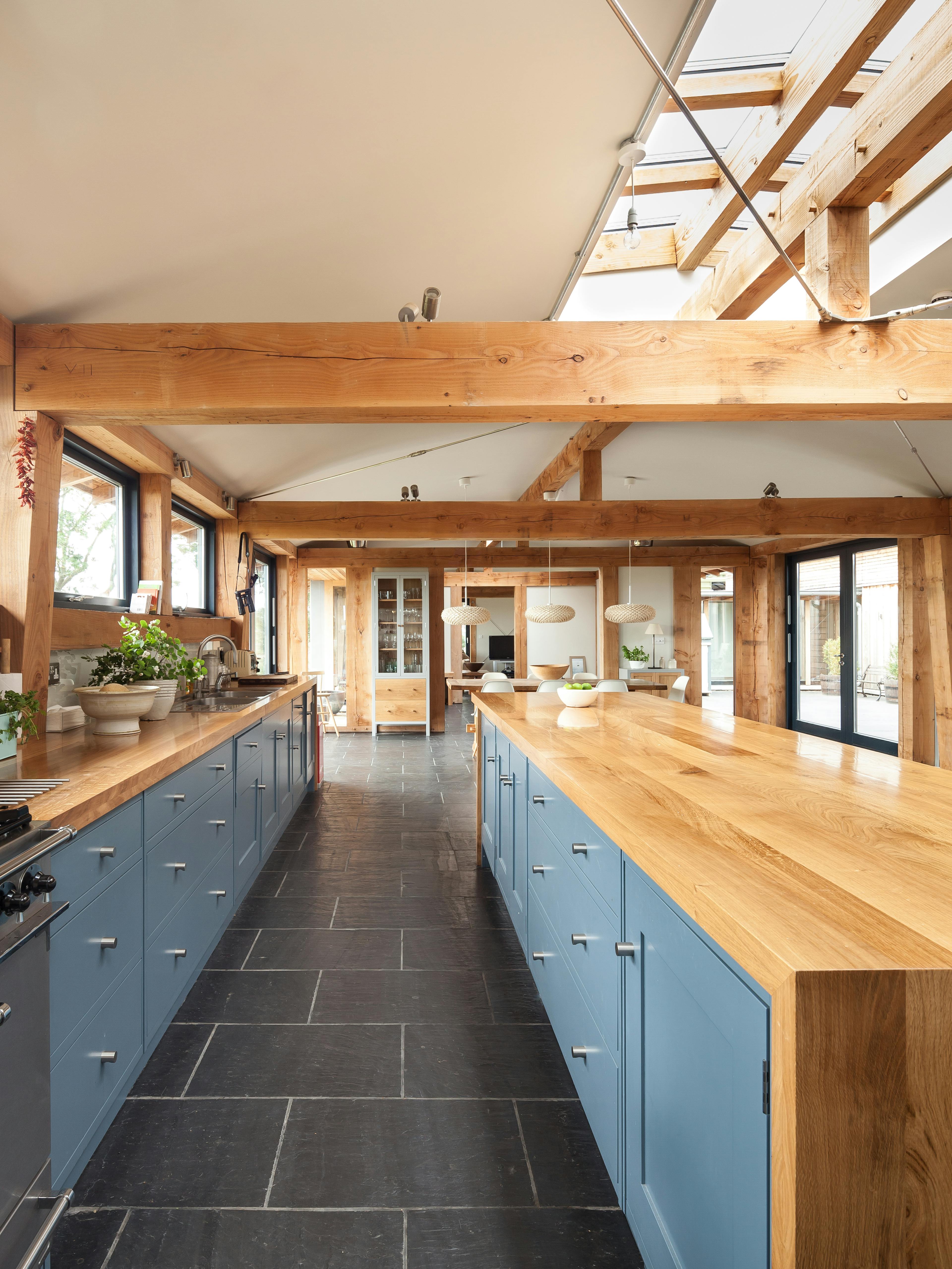 The kitchen in a Douglas fir framed family farmhouse with large dark grey flagstones on the floor and blue grey kitchen cabinets, and a roof lantern