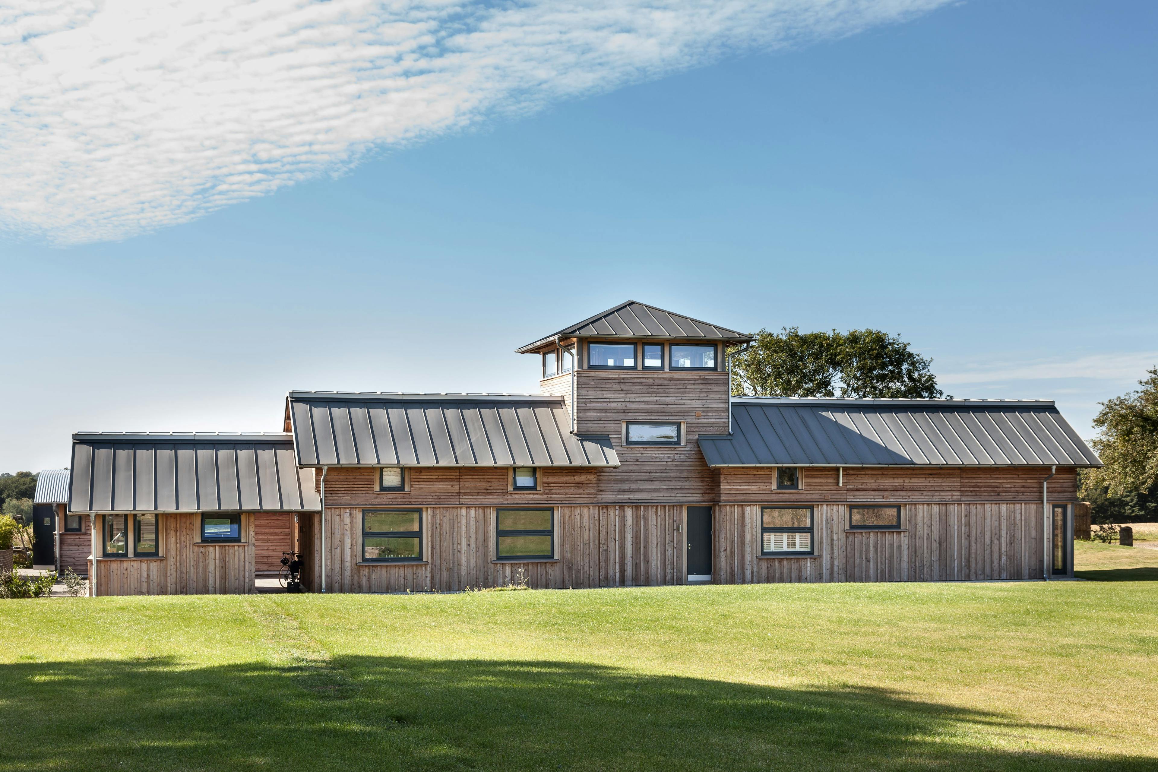 A timber clad large family farmhouse with a tower surrounded by a green lawn
