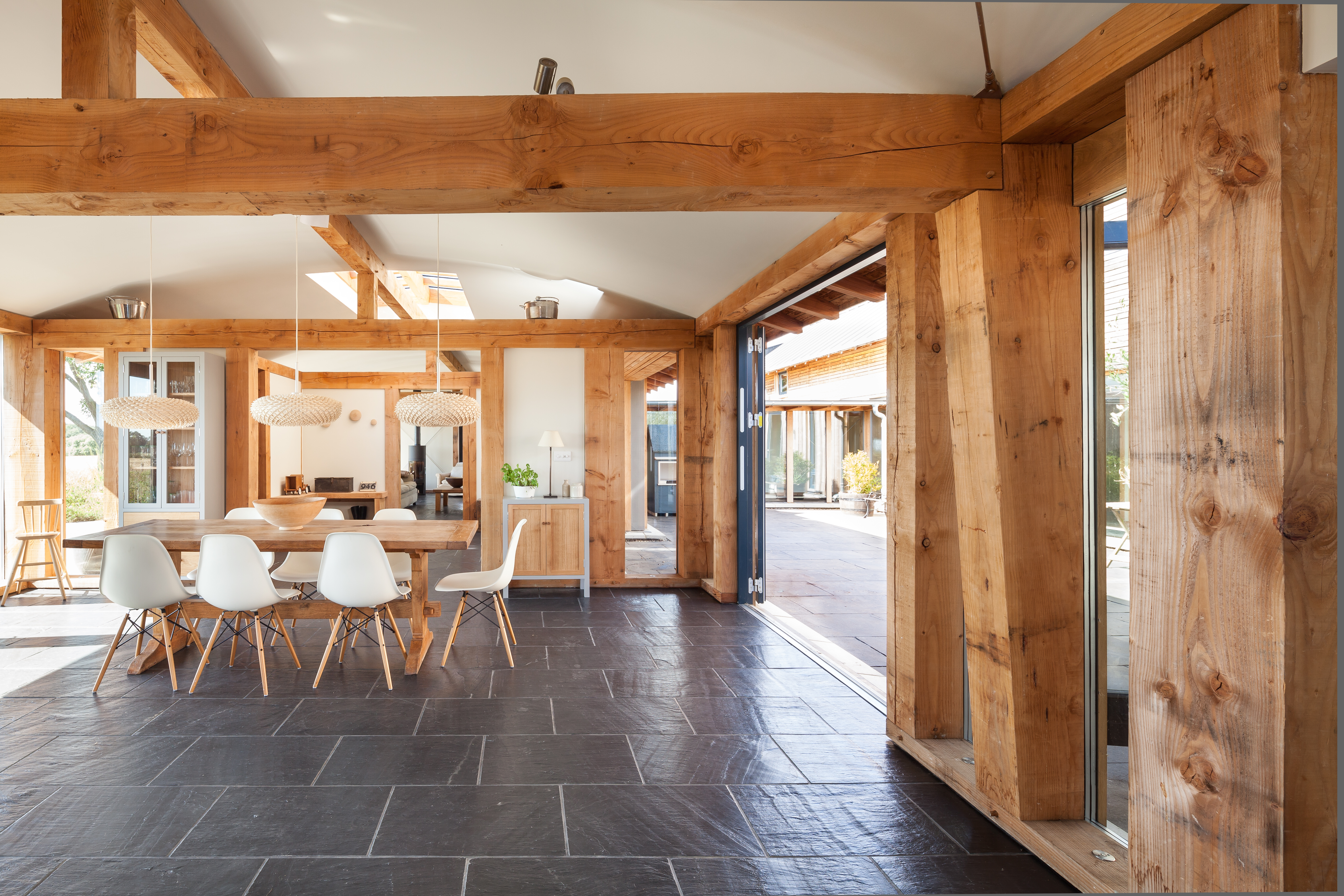 The dining area of a Douglas fir framed family farmhouse with large dark grey flagstone on the floor and bifold doors opening out to a courtyard