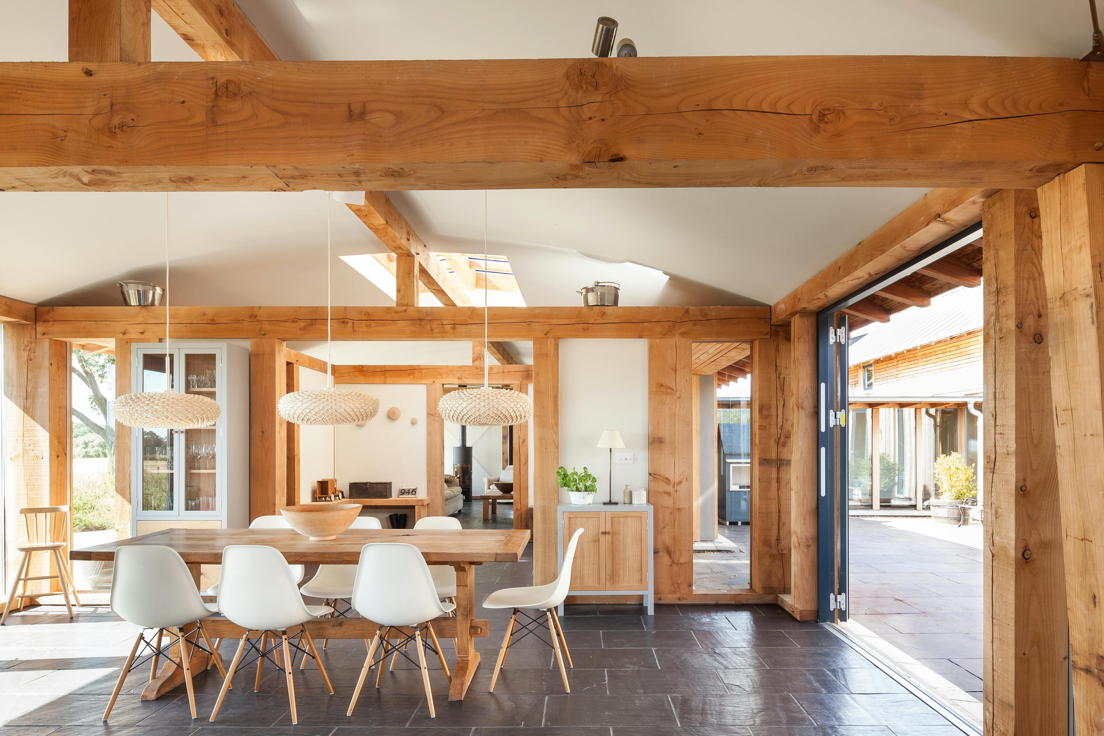 The dining area of a Douglas fir framed family farmhouse with large dark grey flagstone on the floor and bifold doors opening out to a courtyard