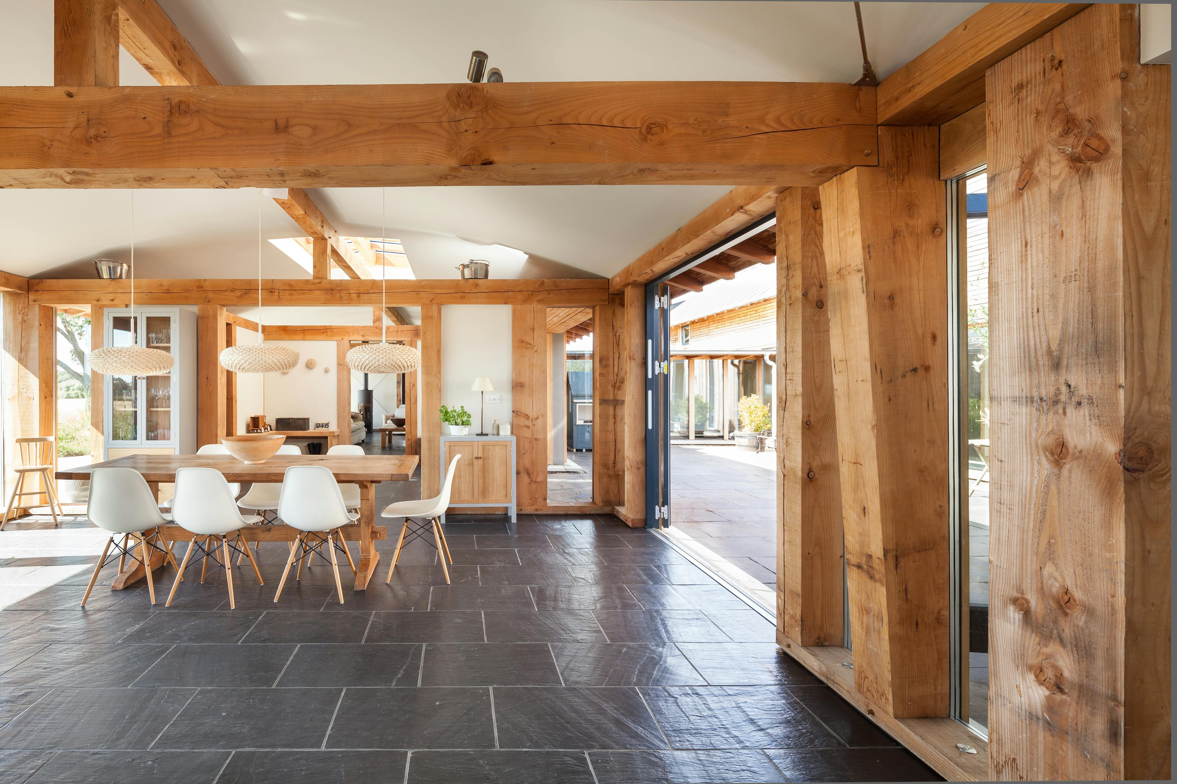 The dining area of a Douglas fir framed family farmhouse with large dark grey flagstone on the floor and bifold doors opening out to a courtyard