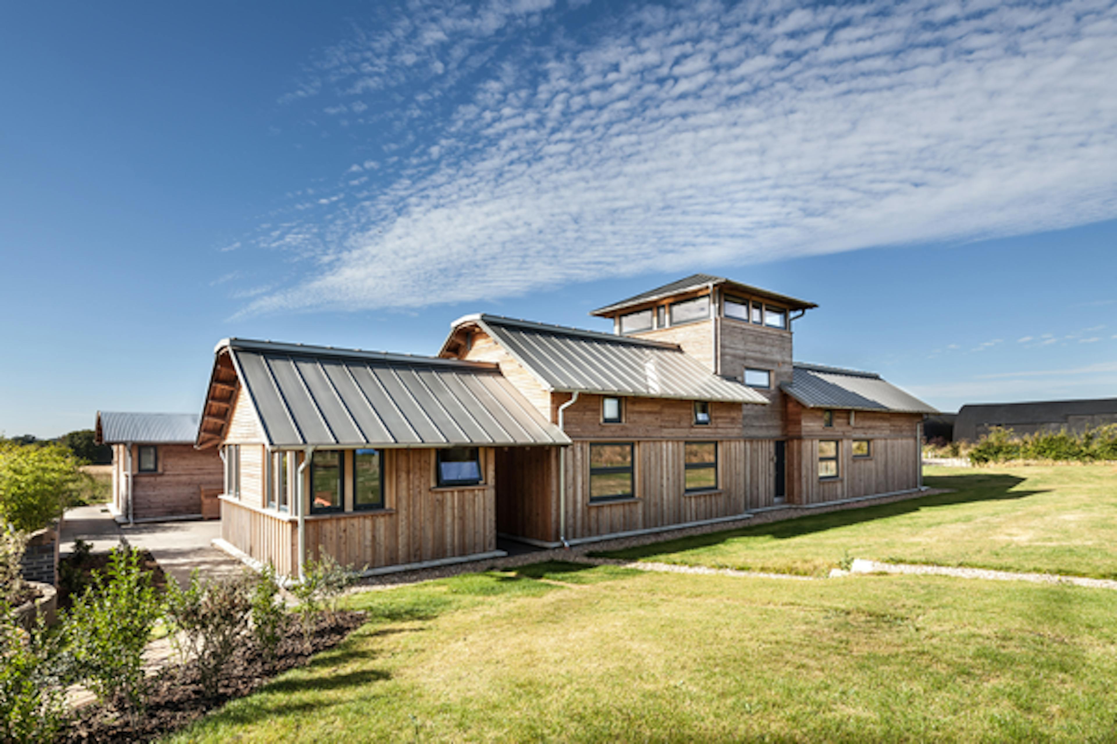The rear of a timber clad large family farmhouse with a tower surrounded by a green lawn