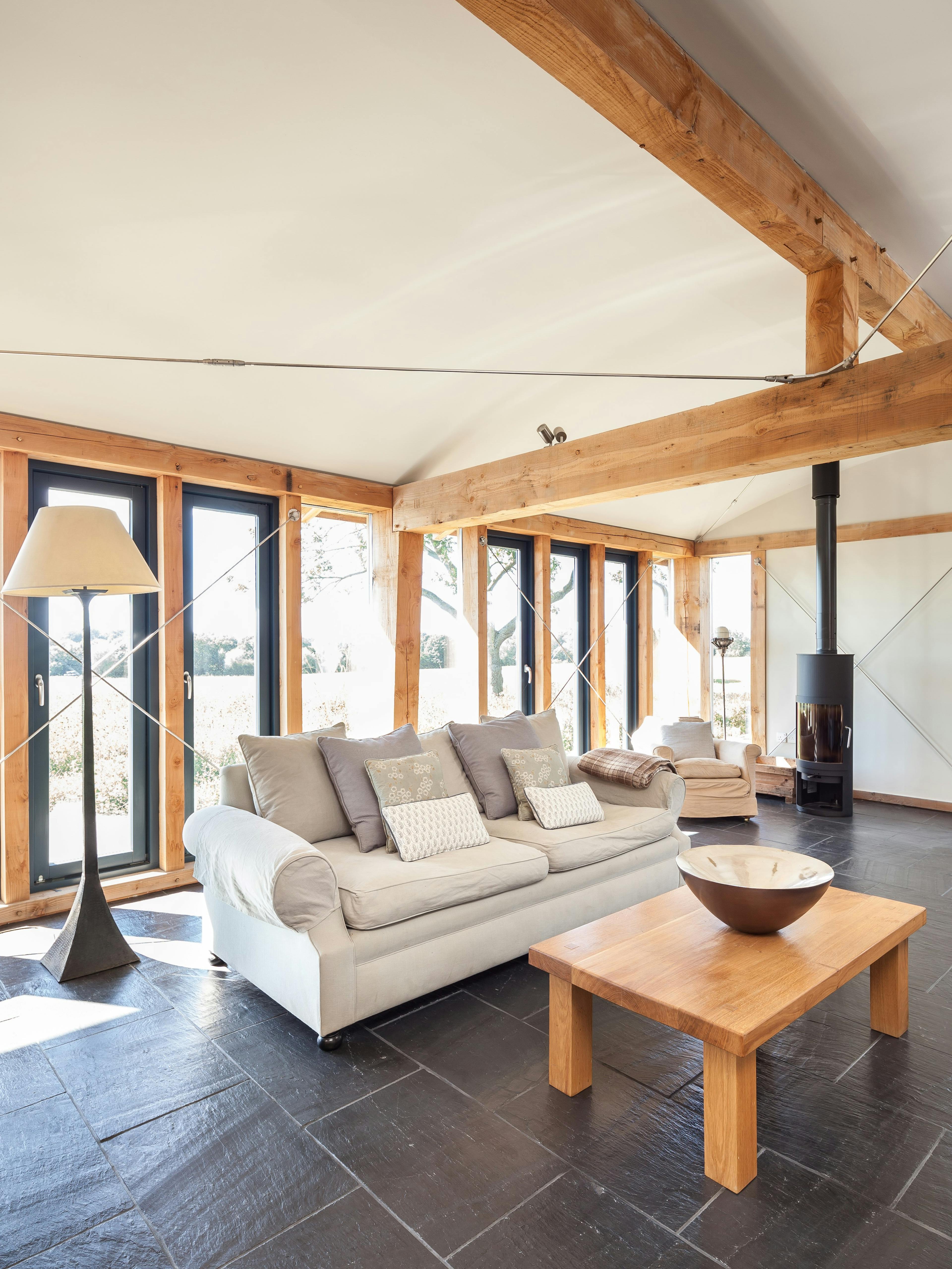 The sitting area in a Douglas fir framed family farmhouse with sofas and log burner and large glazing with views of the garden