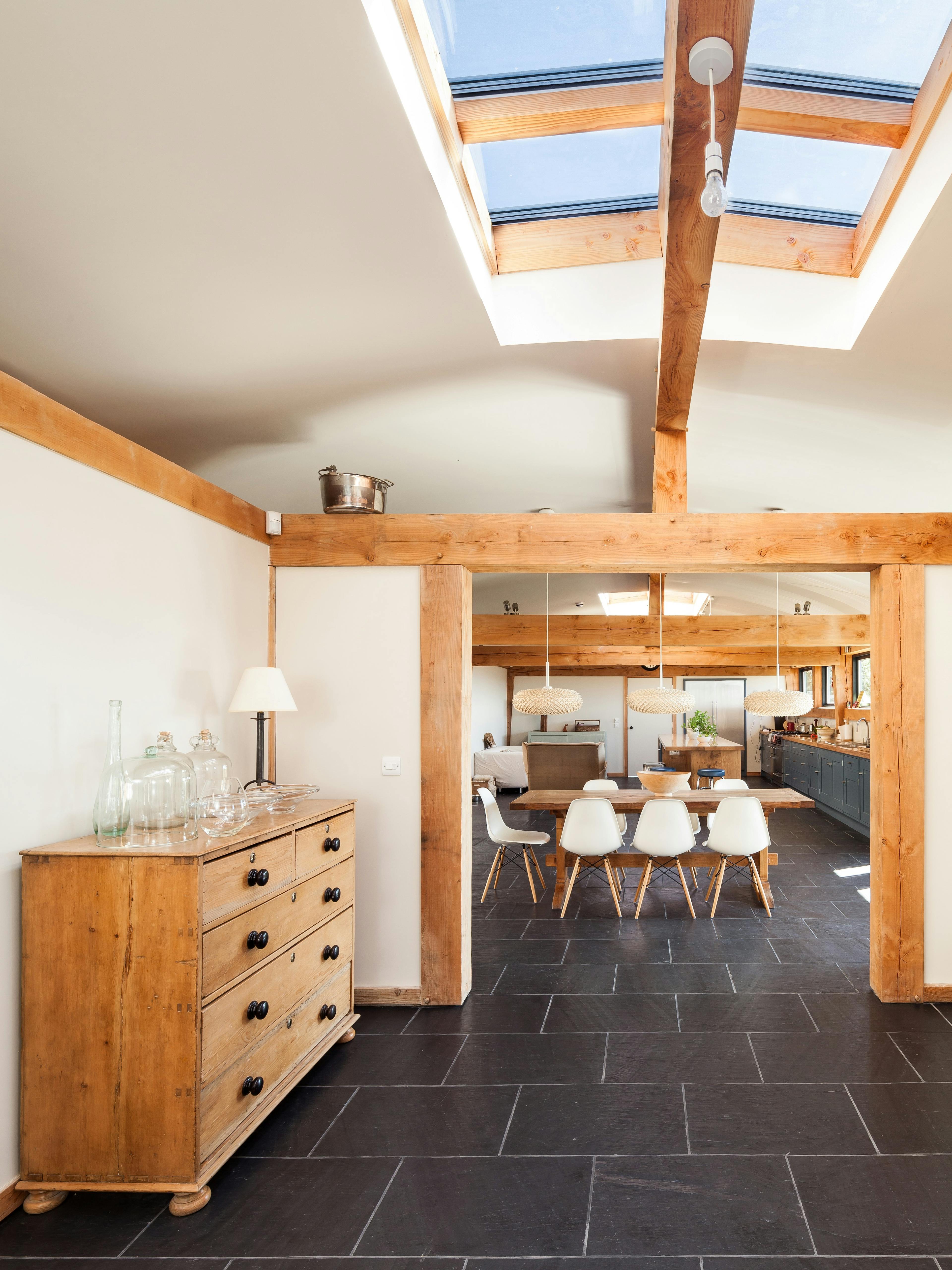 The dining area in a Douglas fir framed family farmhouse can be seen through a doorway with large dark grey flagstones on the floor and a roof lantern in the ceiling