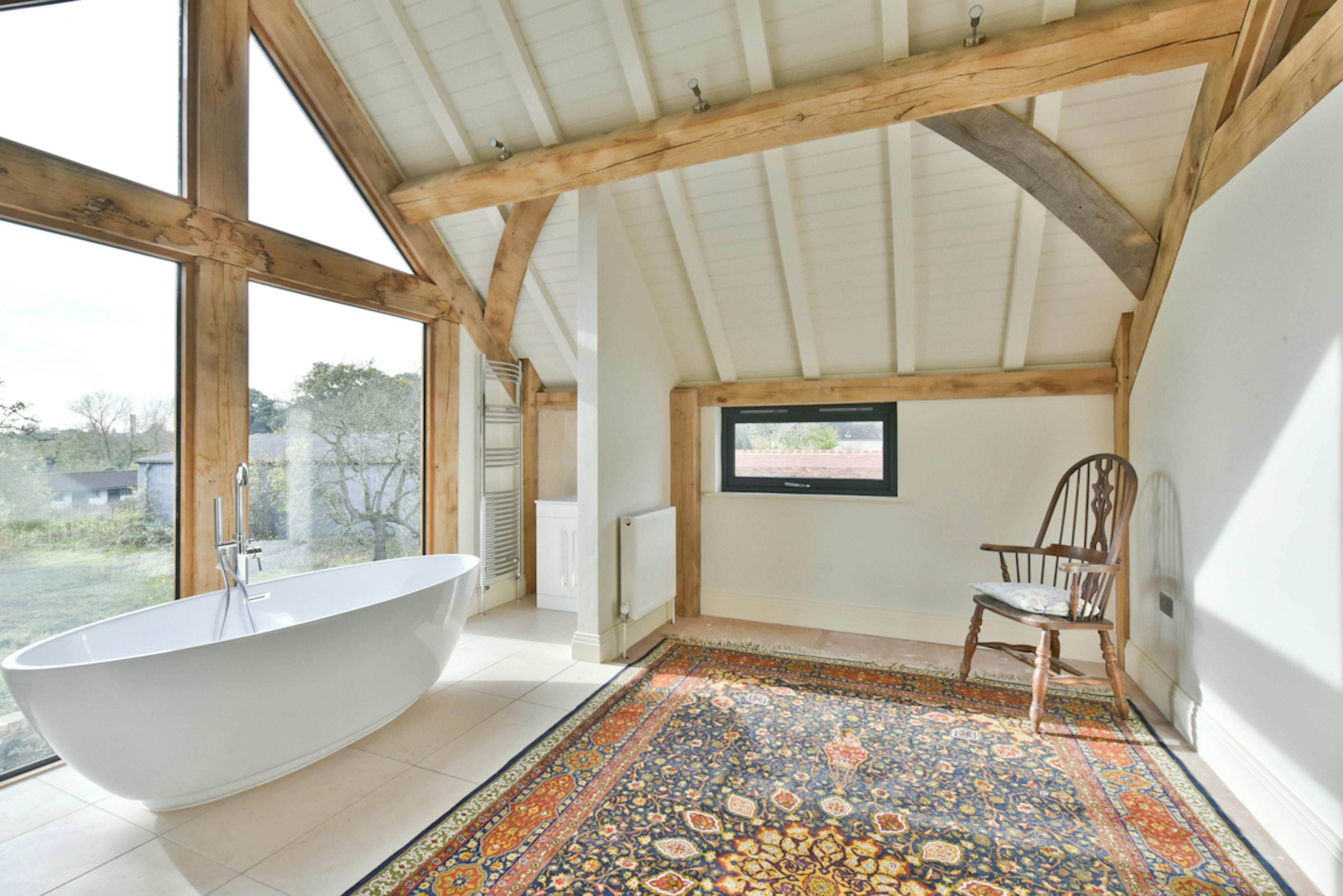 A freestanding bath by a glazed window on the 1st floor of an oak framed extension to a 17th century pub