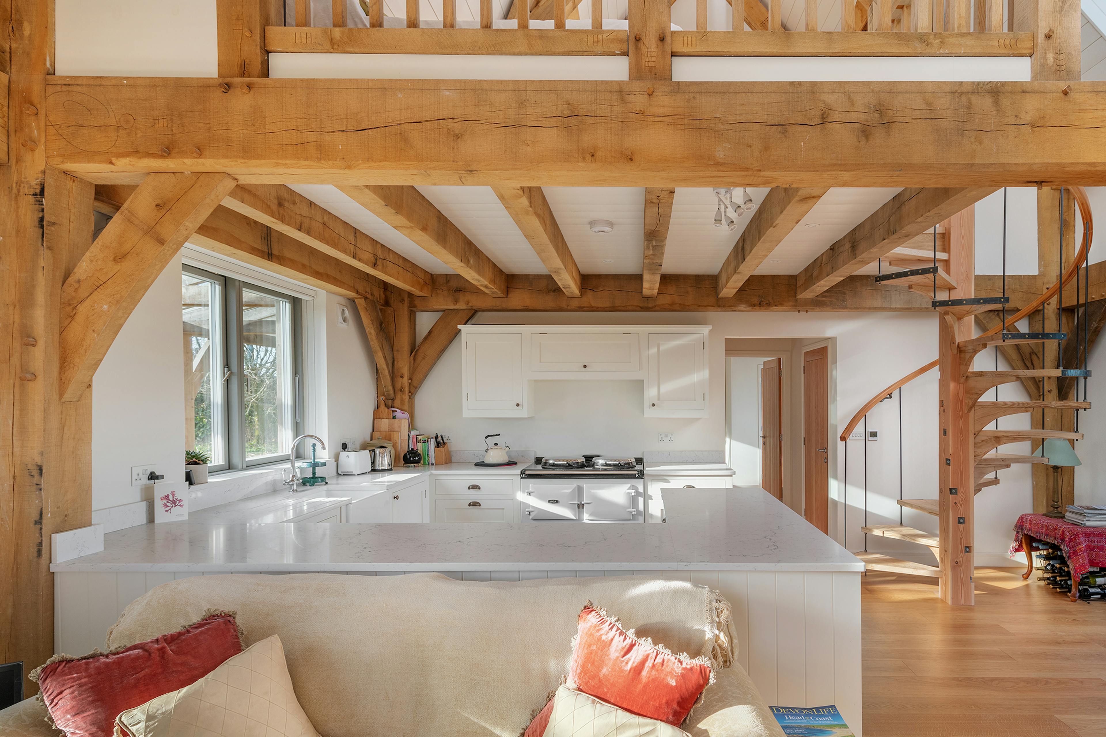A timber wooden spiral staircase, open plan kitchen and sitting area in an oak framed home
