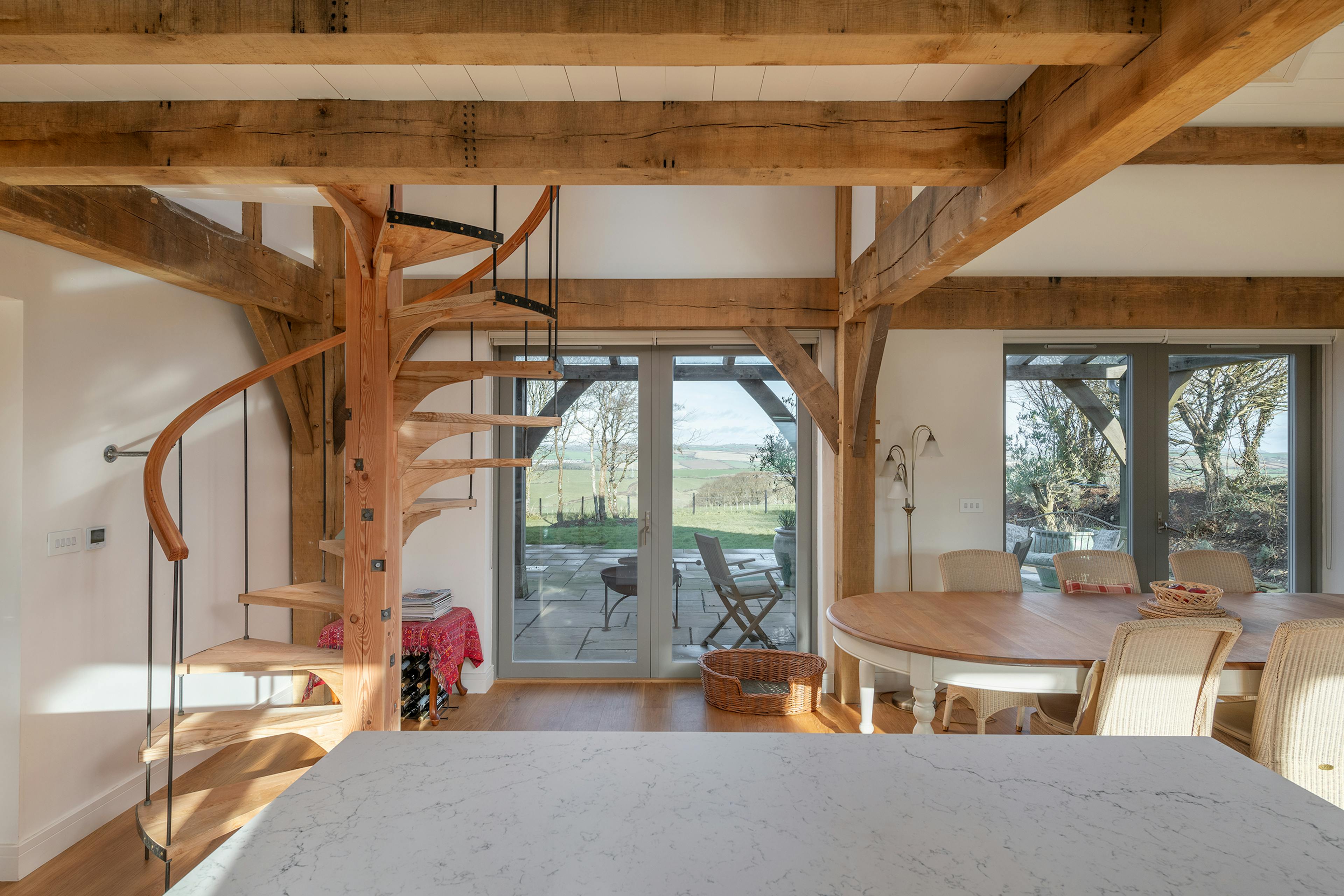 A timber wooden spiral staircase and dining area in an oak framed home