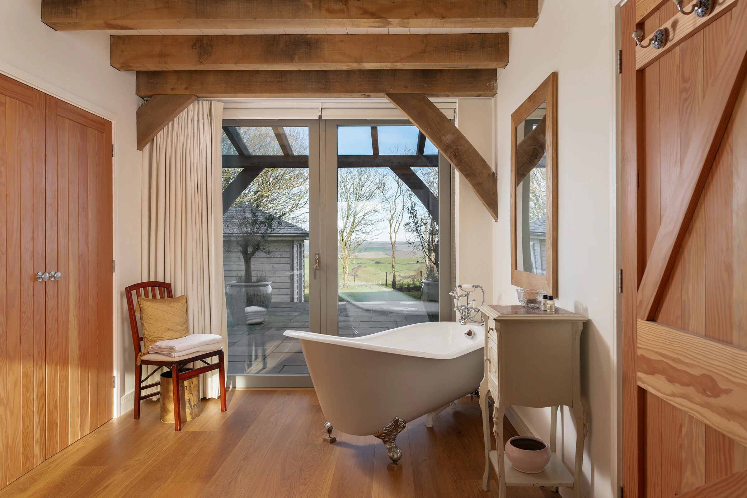 A bath with a white freestanding bath in an oak frame home and doors to a patio and oak frame veranda