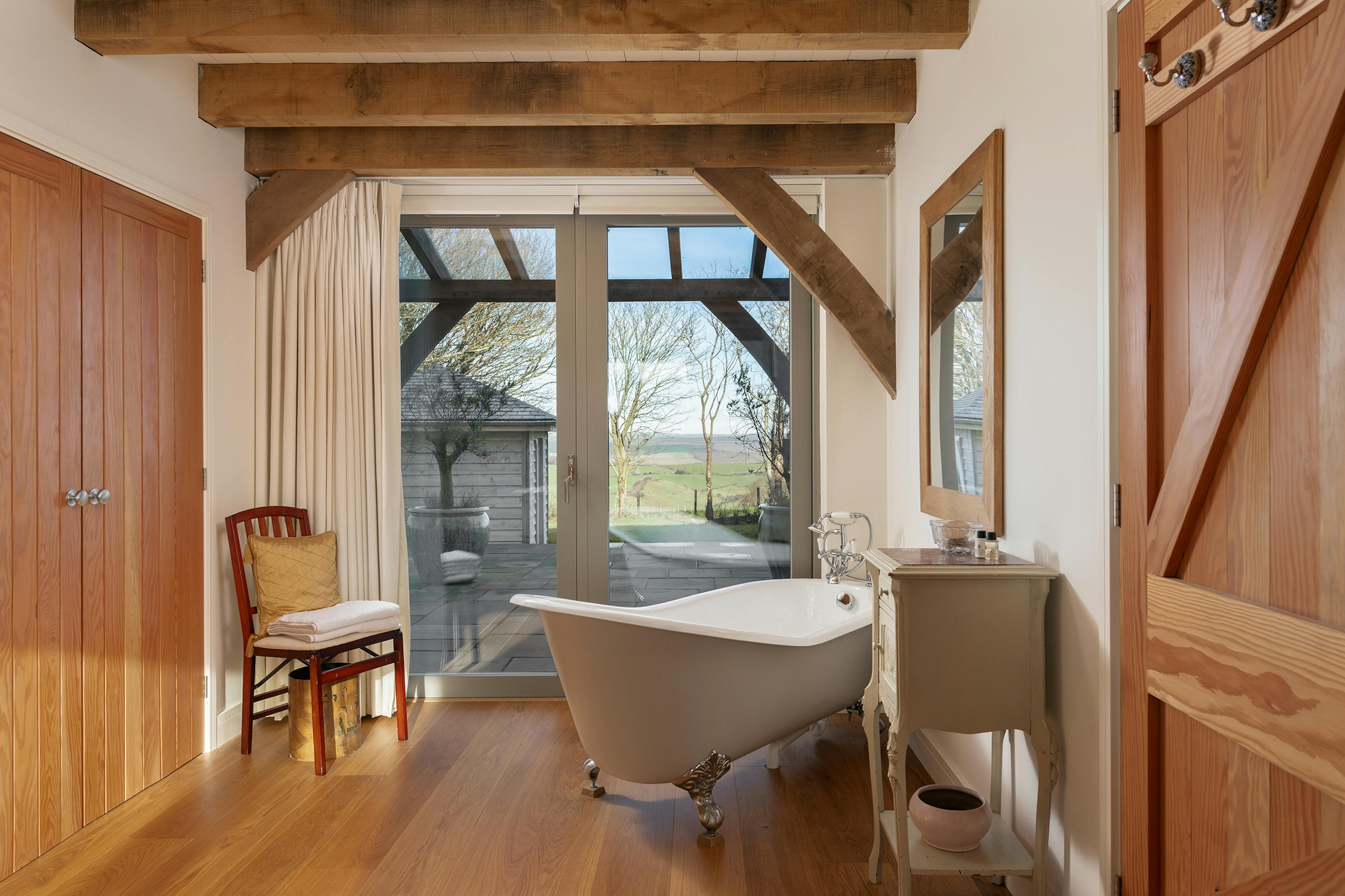 A bath with a white freestanding bath in an oak frame home and doors to a patio and oak frame veranda