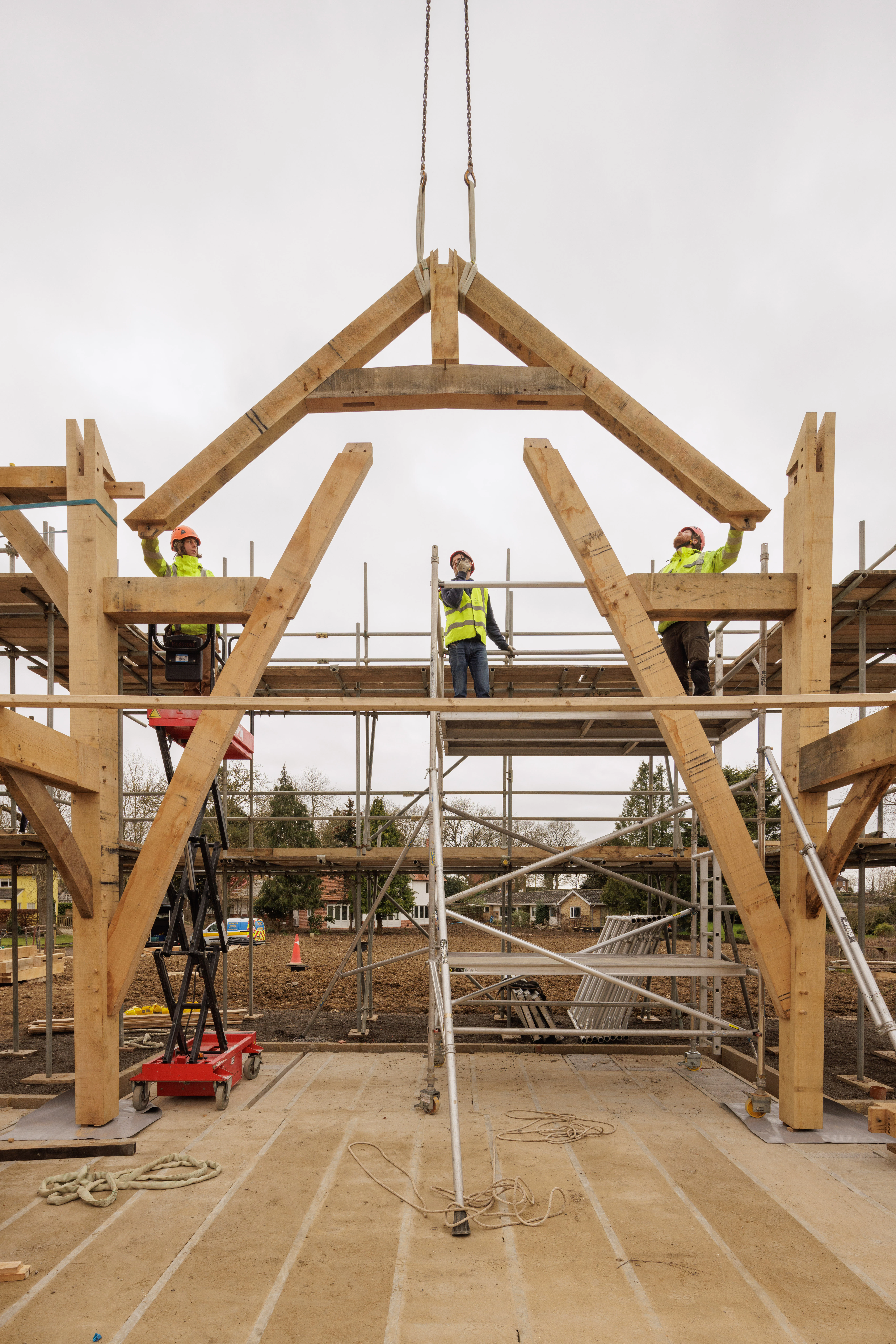 Three carpenters using a crane to lift a piece of oak into place during installation of a large oak frame home
