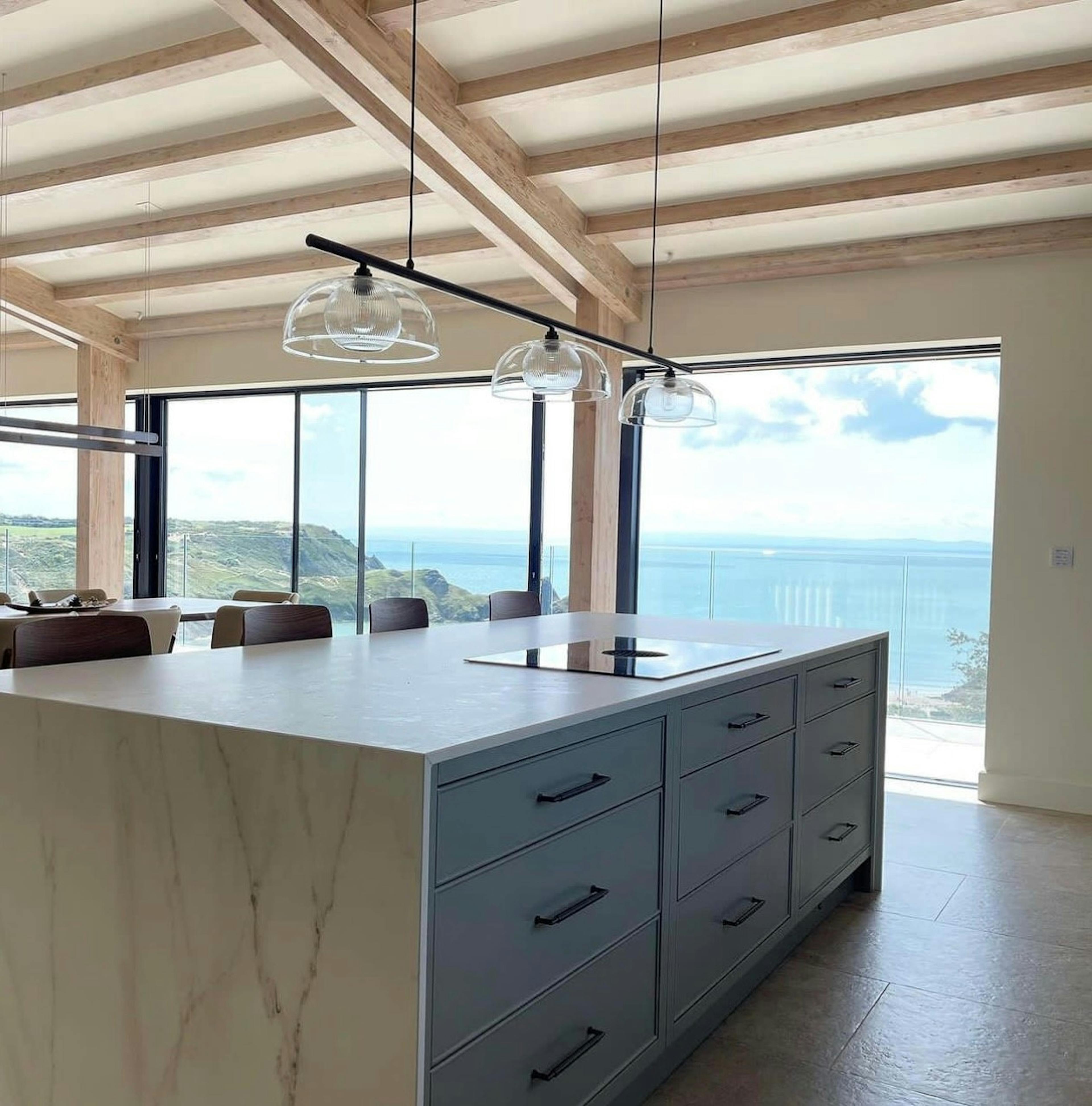 An open plan kitchen dining area of a large modern new build home with a larch glulam mono pitch roof and views of the sea